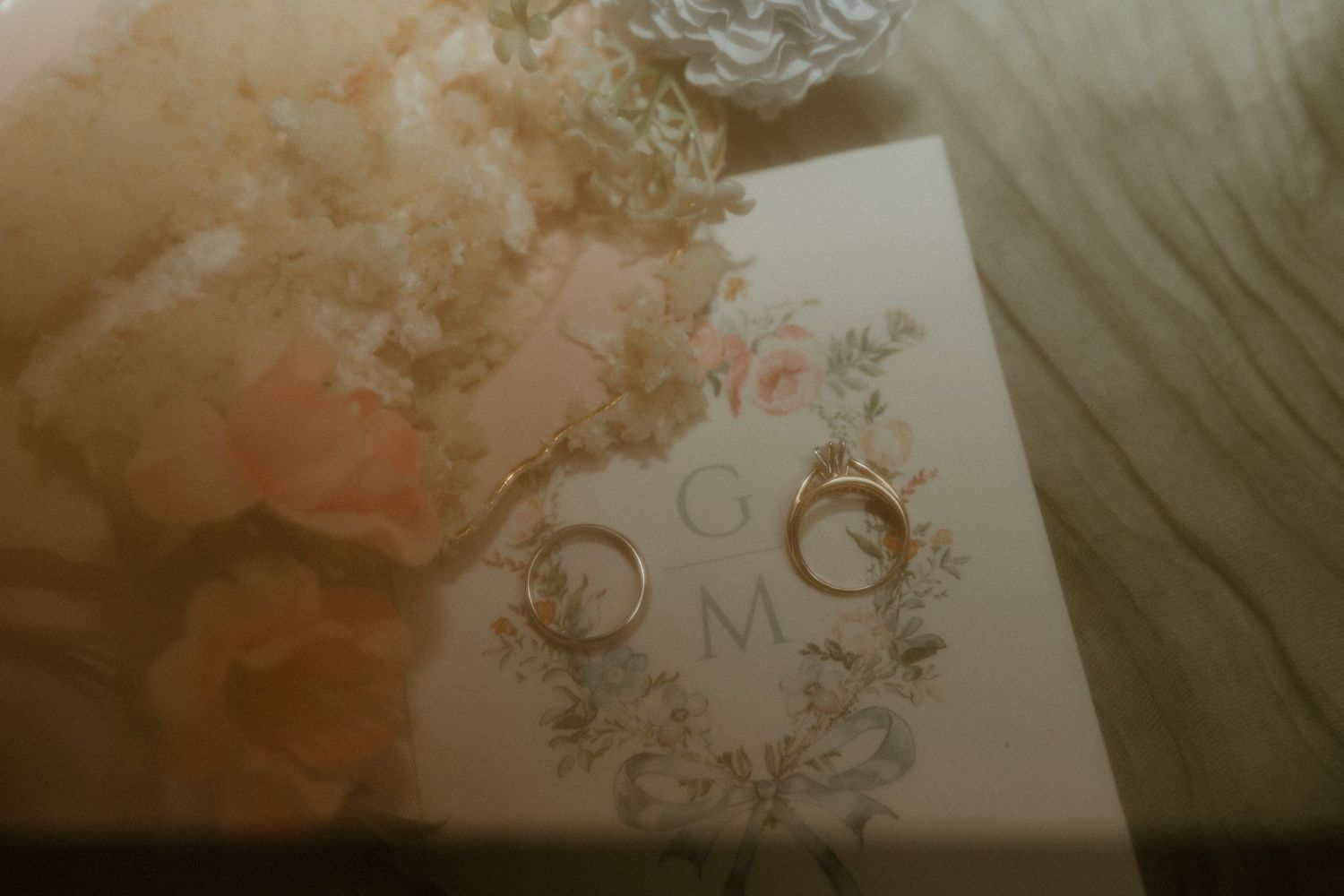 Two gold wedding bands rest on monogrammed wedding stationery with soft floral details.