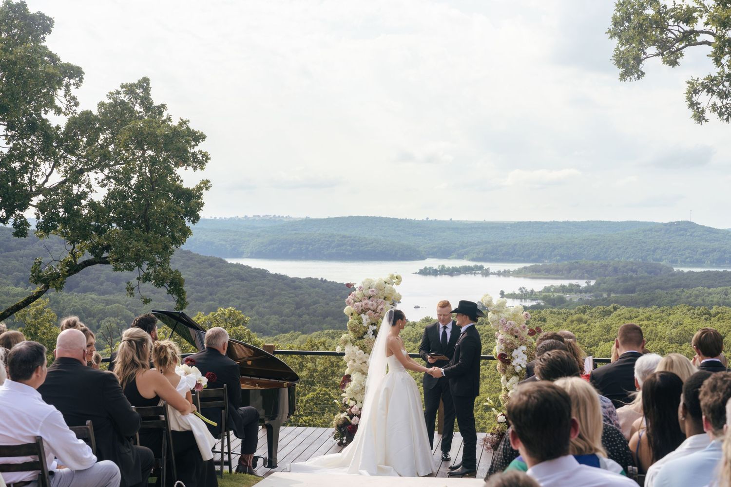 Panoramic view of a mountain wedding ceremony with guests seated on a wooden deck.