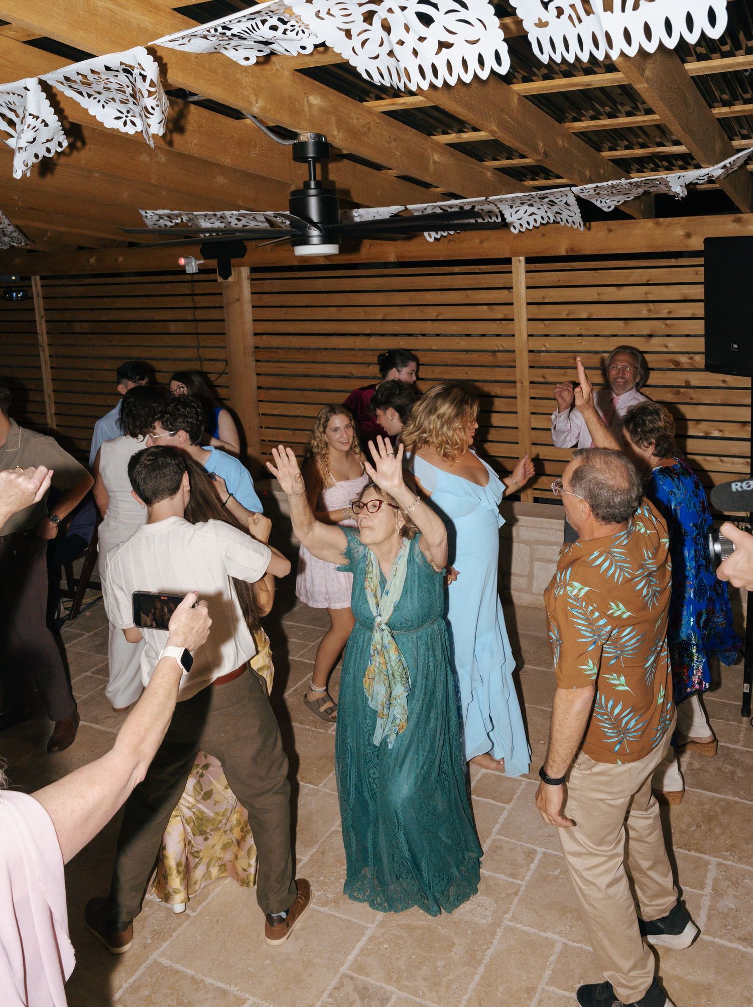 Wedding guests dancing and celebrating on a rustic wooden dance floor under papel picado decorations.