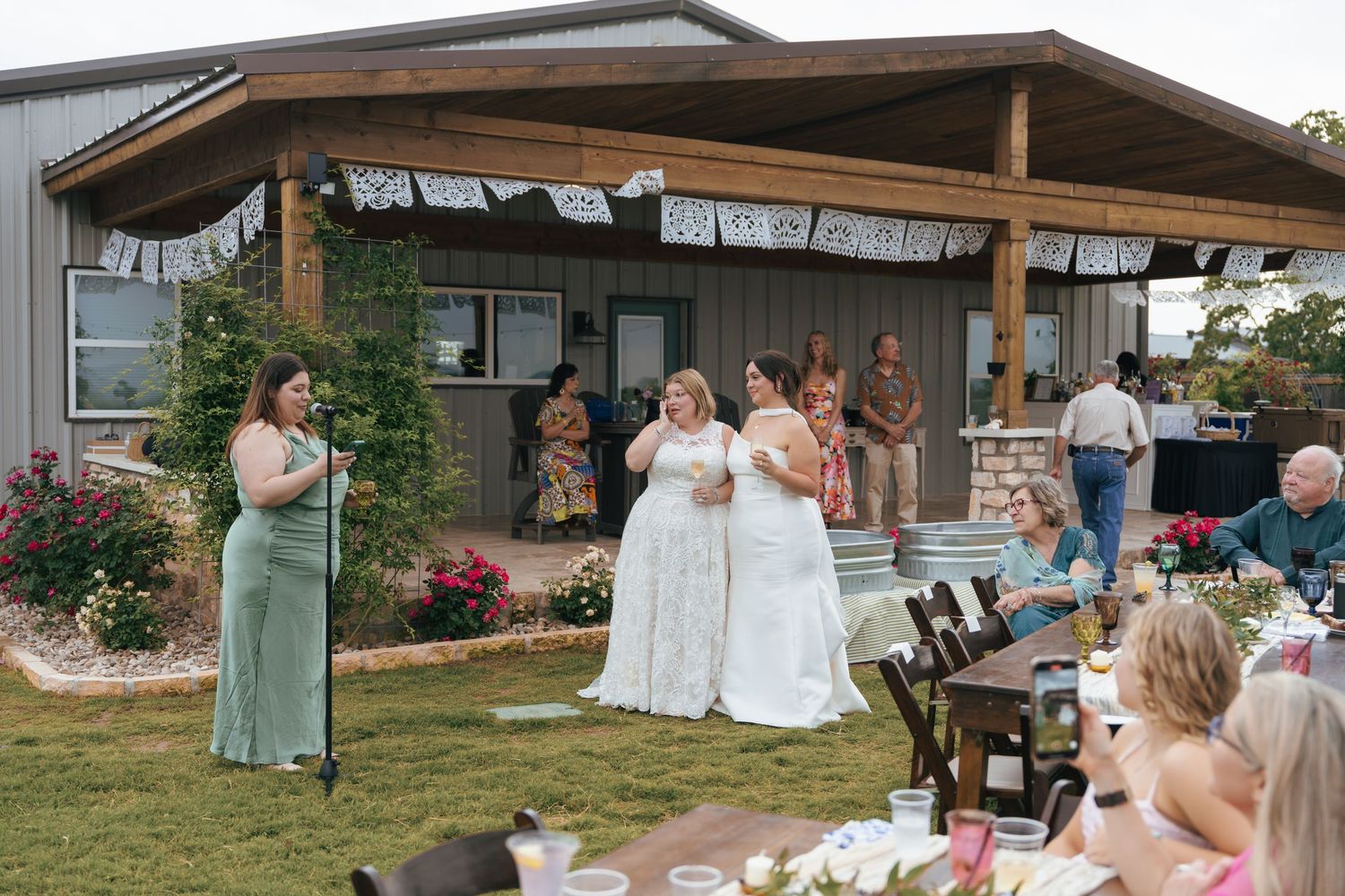 Wedding ceremony guests seated under wooden pavilion during outdoor celebration at rustic venue.