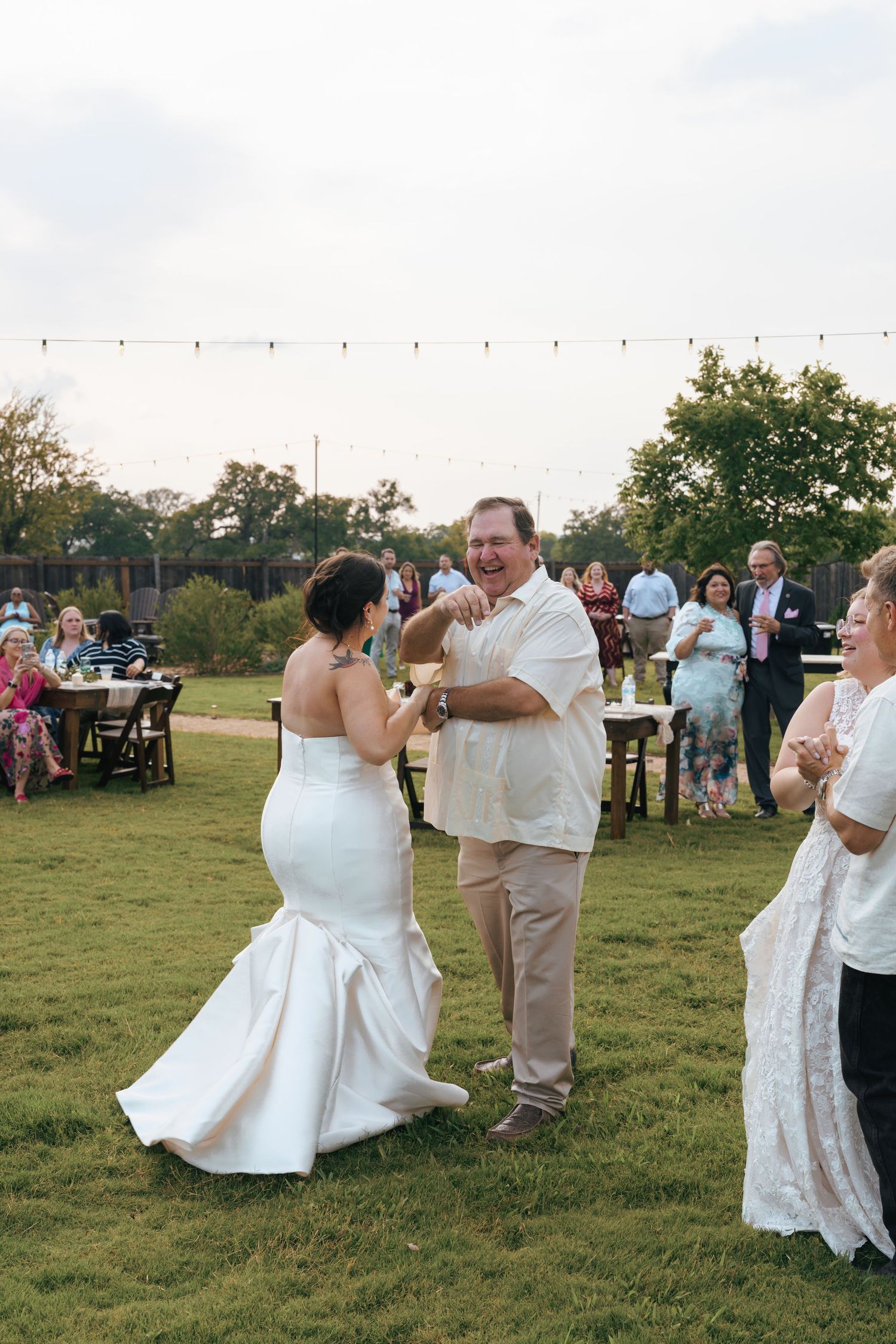 Guests enjoying an outdoor wedding reception on a grassy field with string lights overhead at dusk.