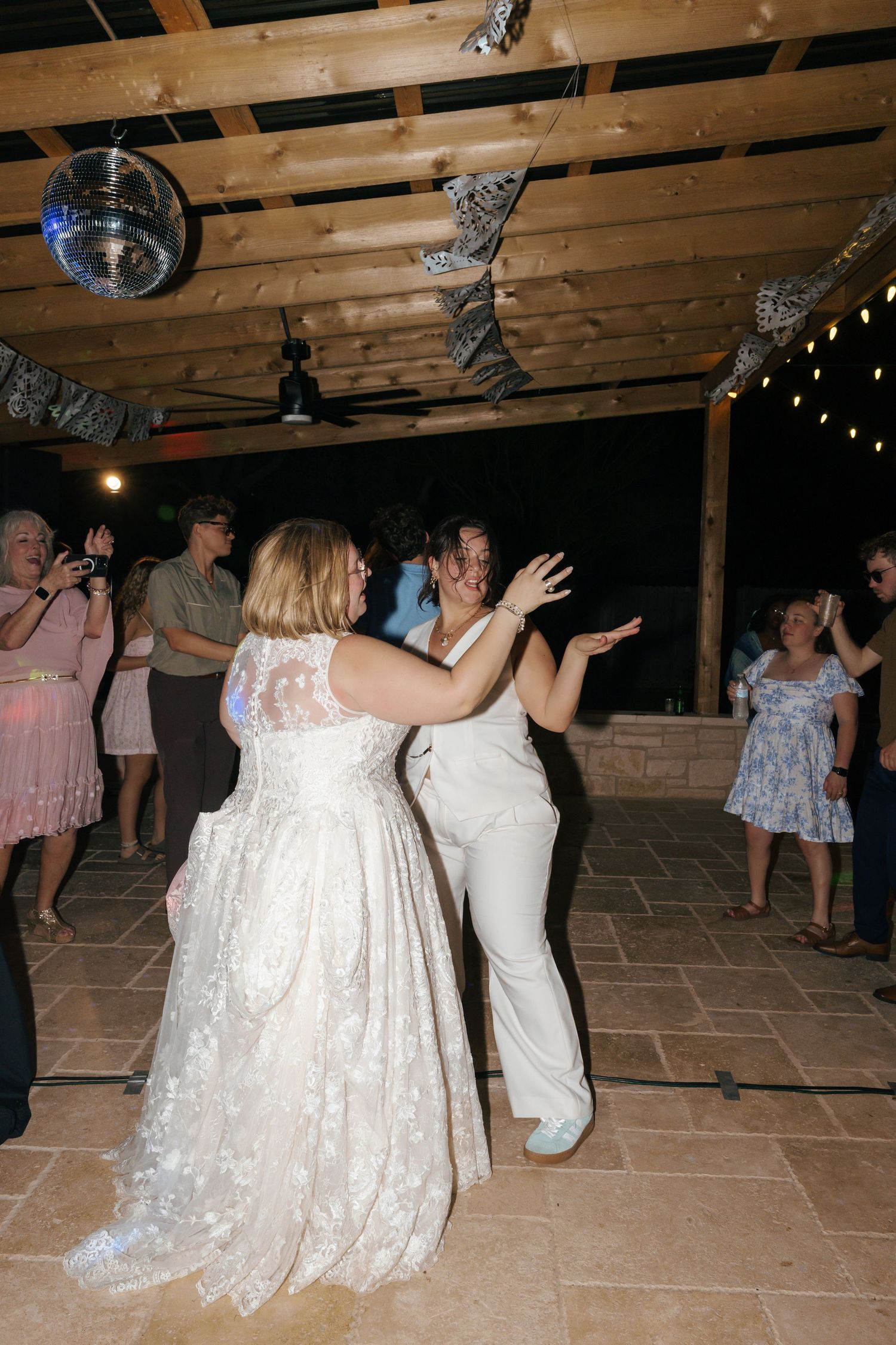 Wedding guests dance and celebrate on a rustic wooden dance floor under string lights.