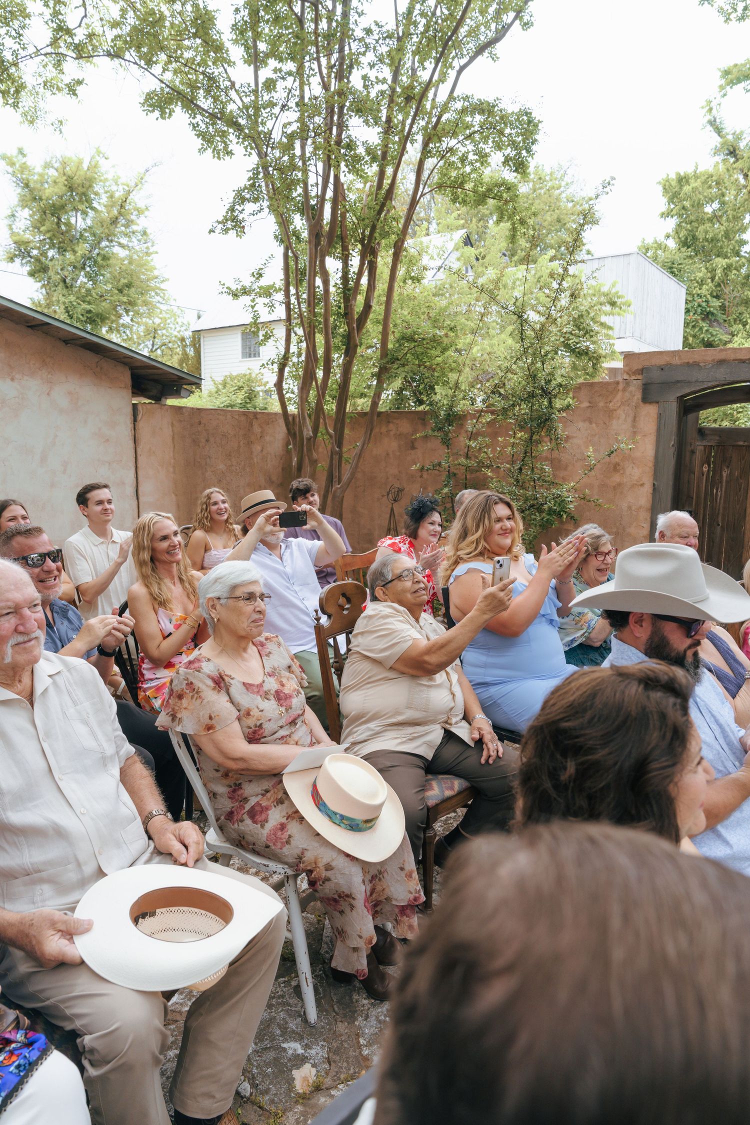 A joyful crowd of wedding guests dancing and celebrating outdoors near brick buildings on a sunny day.