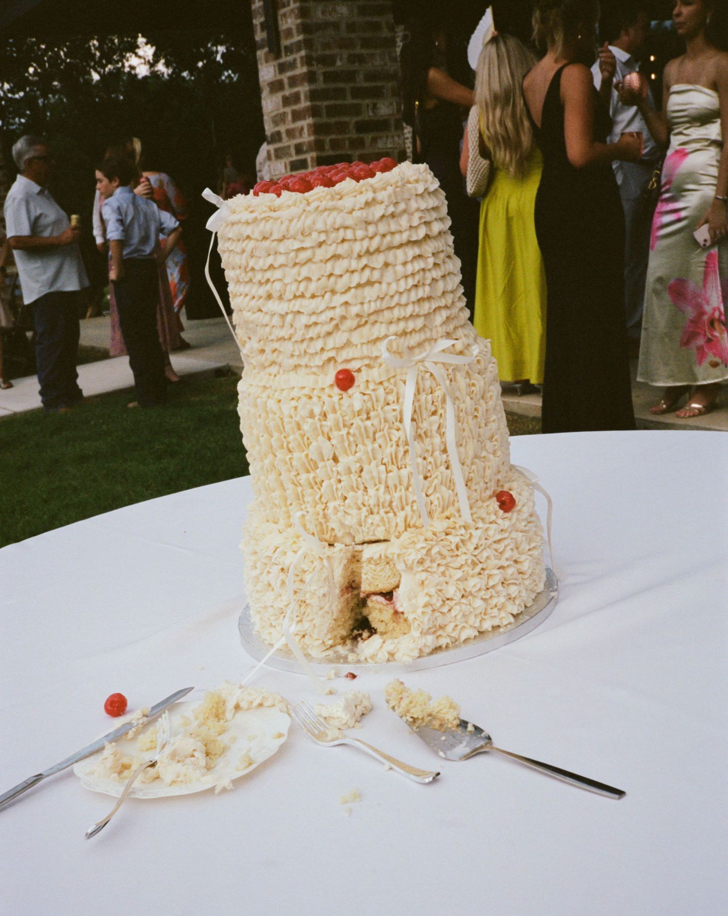 White textured wedding cake with rustic design displayed on outdoor table with scattered crumbs.