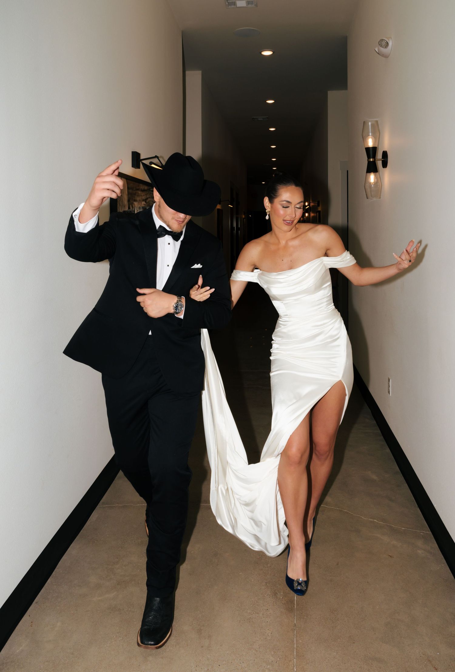 Newlyweds share a fun dance moment in an elegant corridor.
