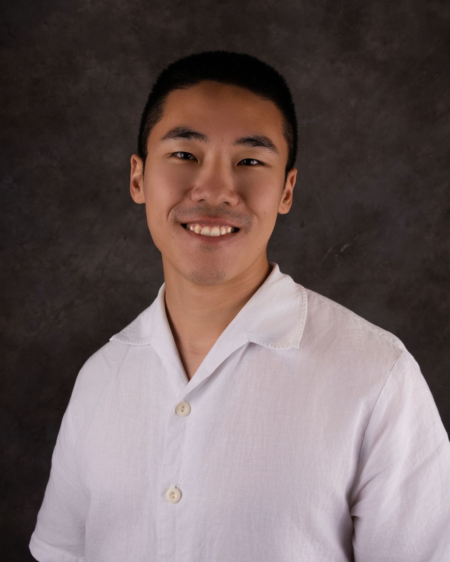Professional headshot portrait of someone in a white button-down shirt against a dark background.