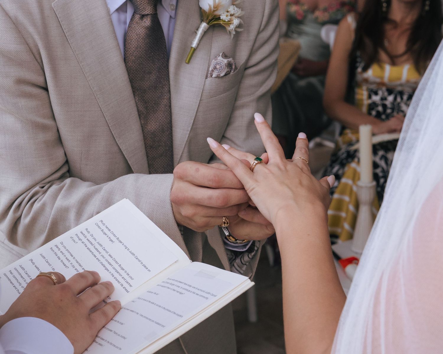 A couple signing marriage documents at a wedding ceremony with hands holding pens over paperwork.