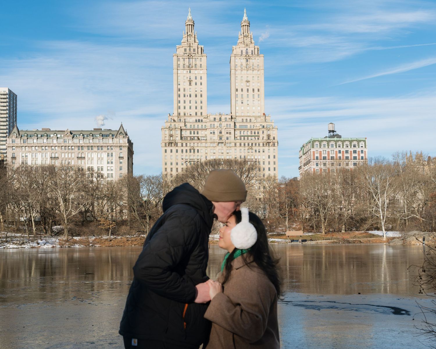 A romantic winter scene with iconic New York City buildings visible across a frozen lake.