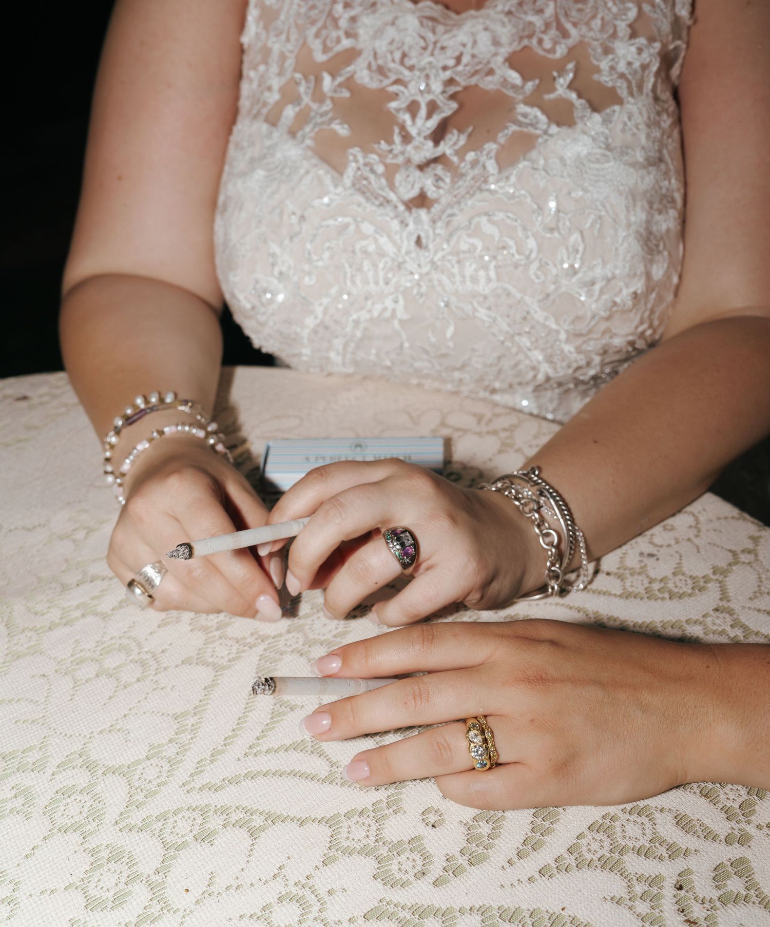 Close-up view of hands wearing delicate lace and jewelry showing intricate details of a wedding dress.