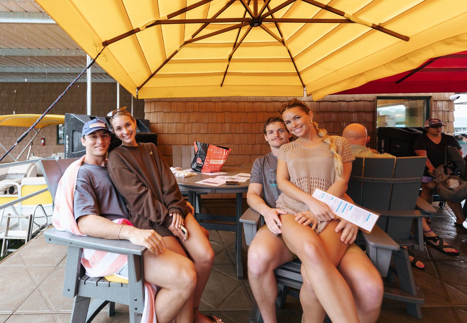 People relax and socialize at an outdoor restaurant patio under yellow umbrellas on a sunny day.