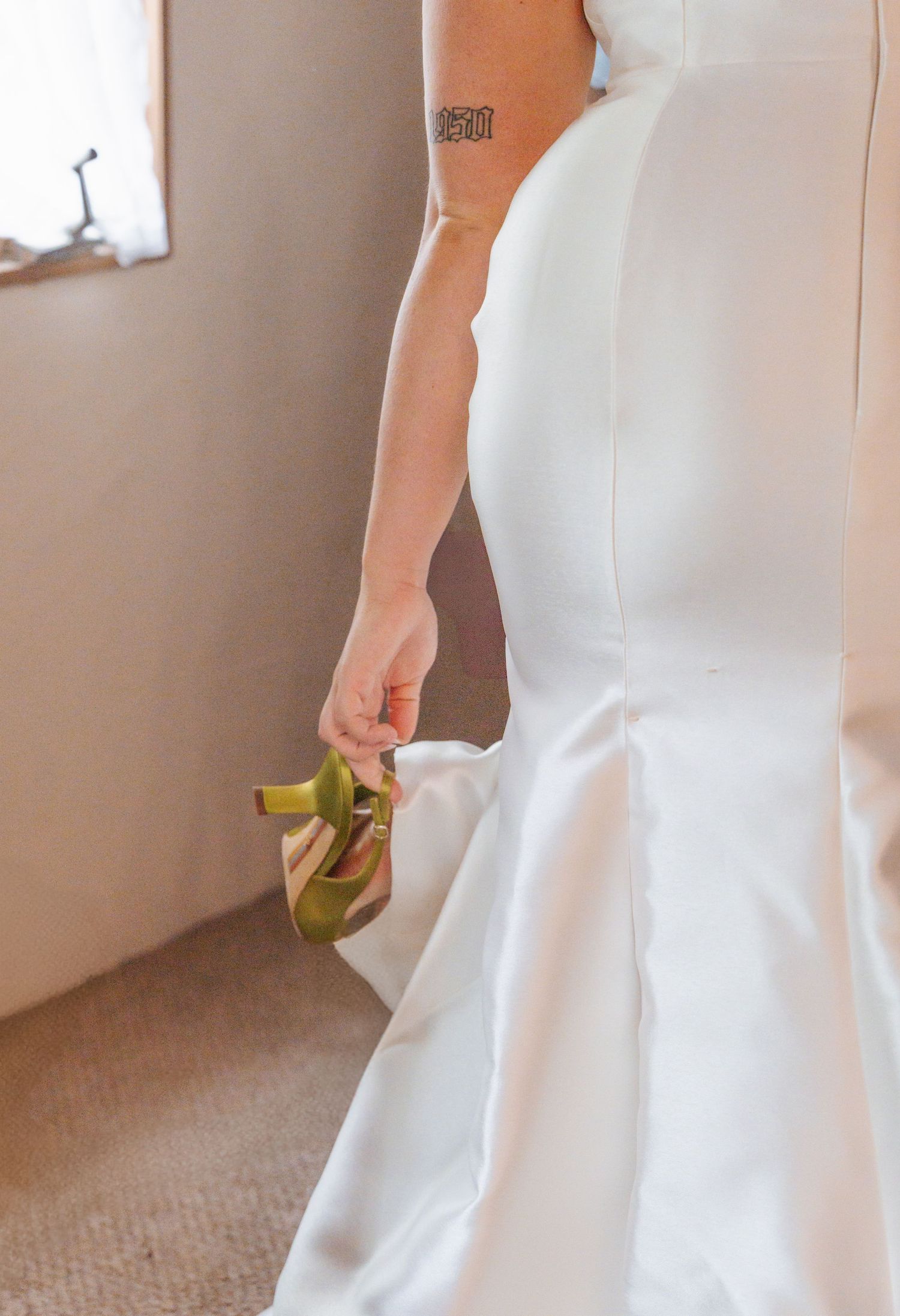 A person in a white wedding dress holding a green apple against a neutral beige wall and carpeted floor.