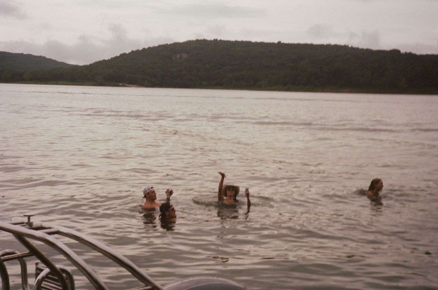 A group of people swimming and playing in a lake surrounded by mountains on a cloudy day.