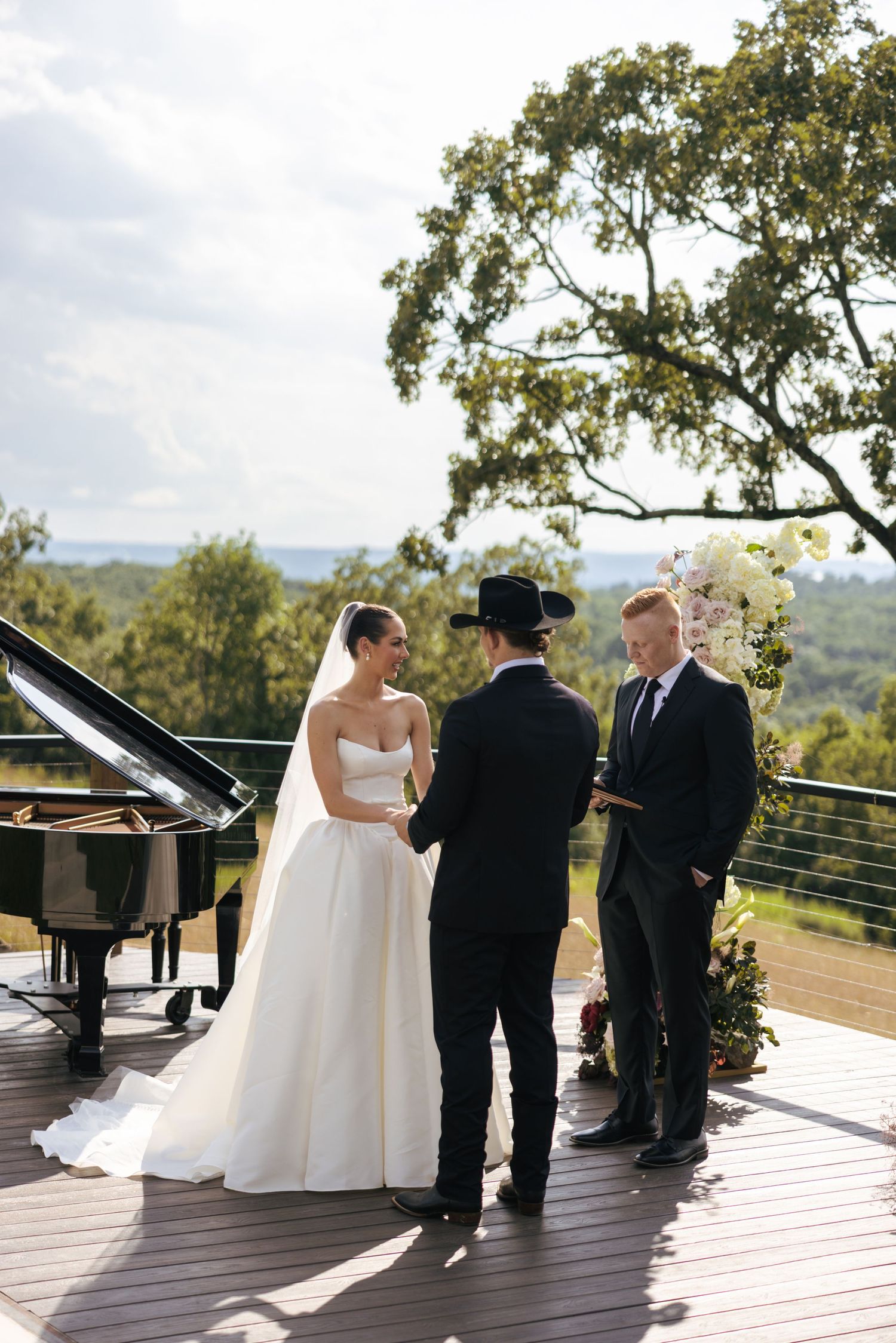 Wedding ceremony unfolds on a wooden deck with scenic mountain backdrop and floral decor.