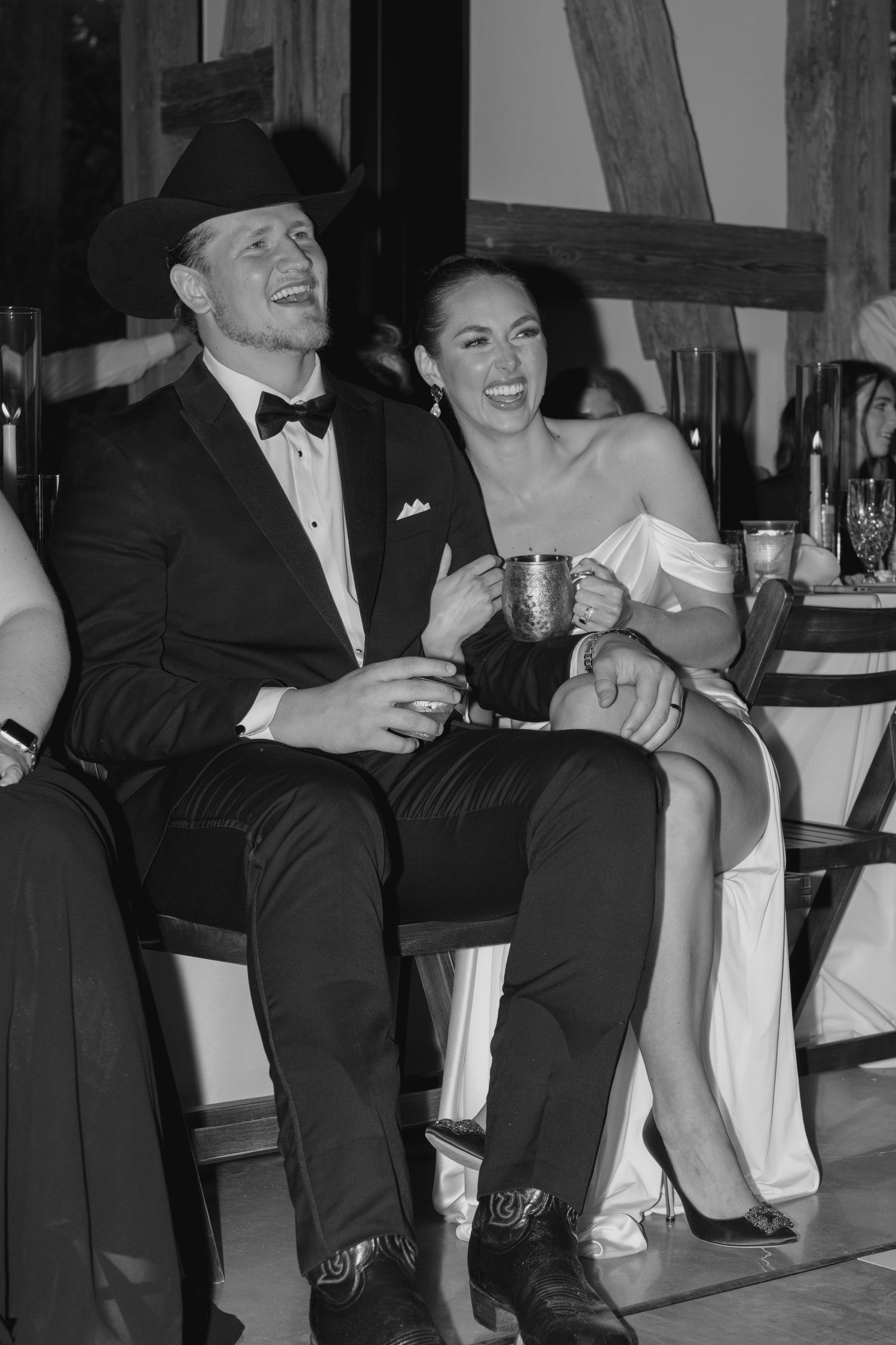 Wedding guests enjoying drinks and laughter during reception in black and white.