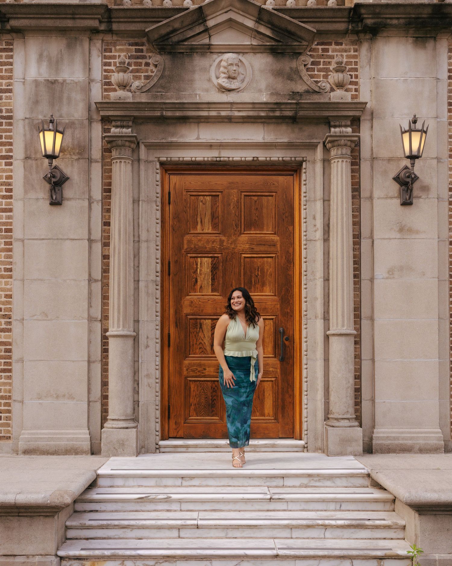 A person in a blue dress poses gracefully on white stone steps in front of wooden church doors.
