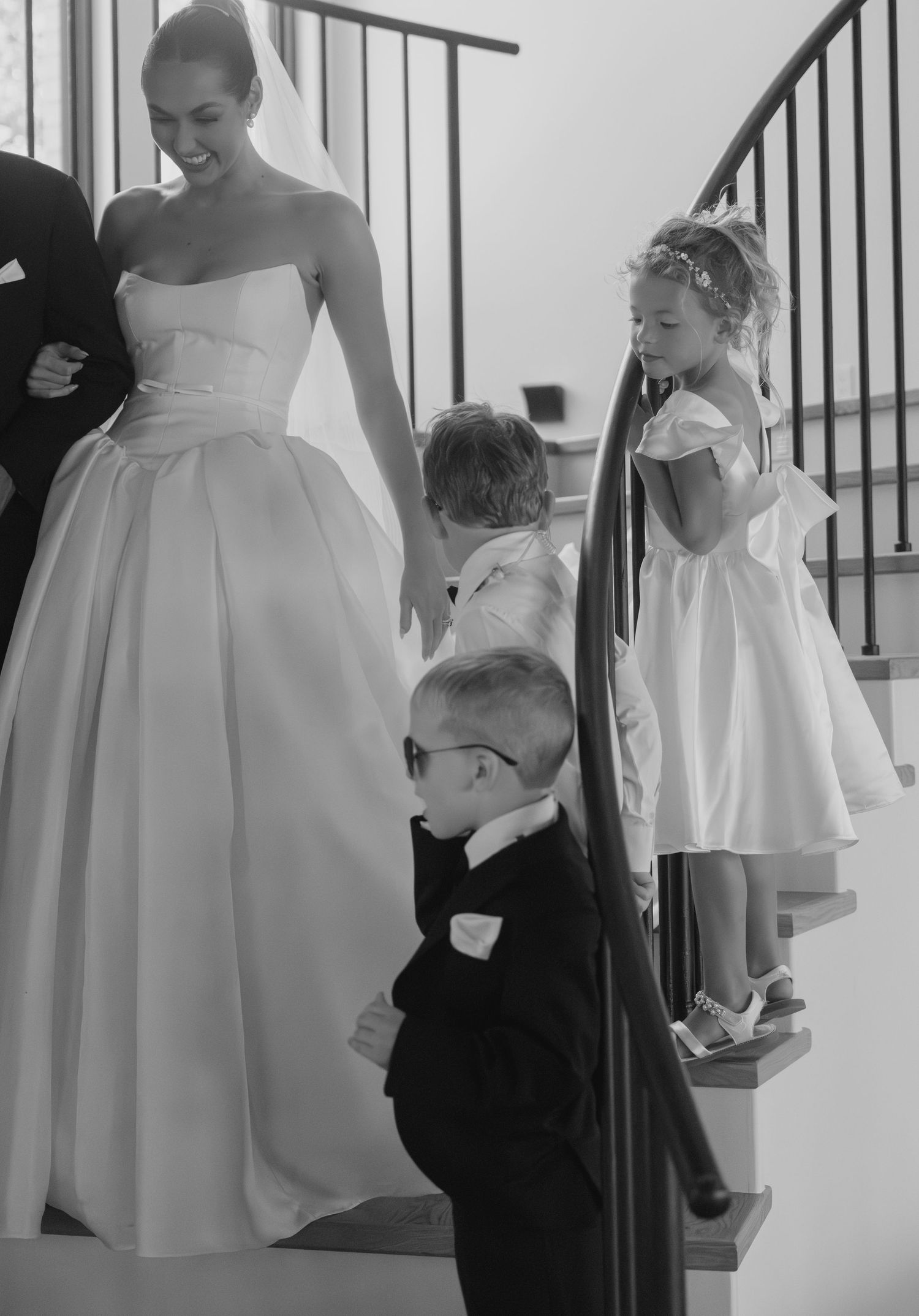 Young attendants in formal wear gather on white stairs during wedding preparations.