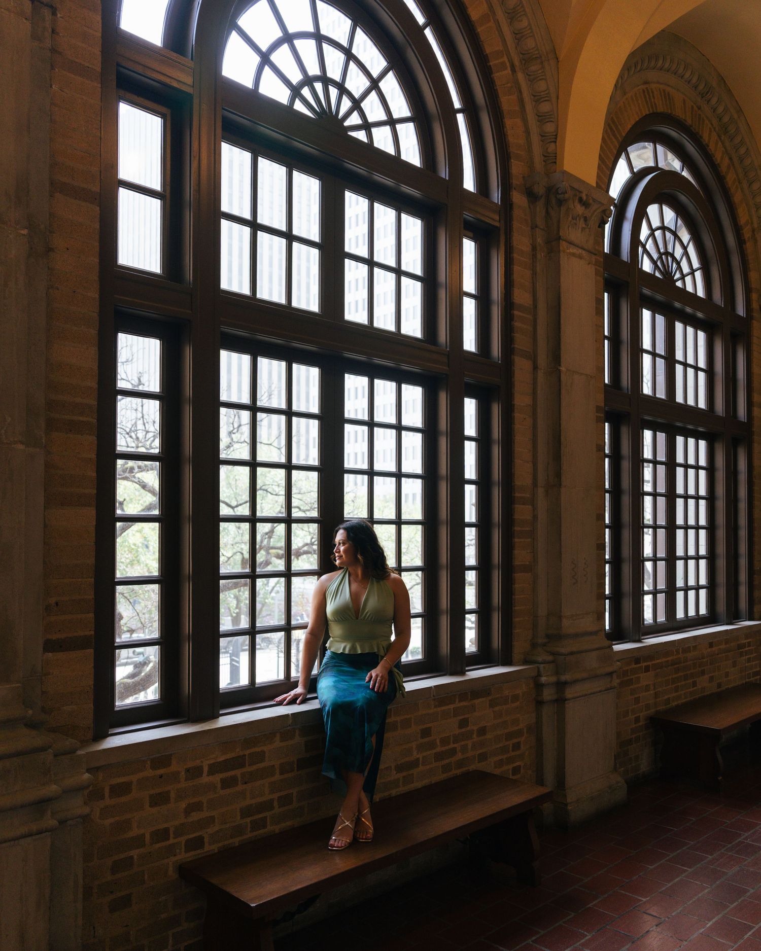 A series of arched windows with sunlight streaming in along a historic brick corridor.