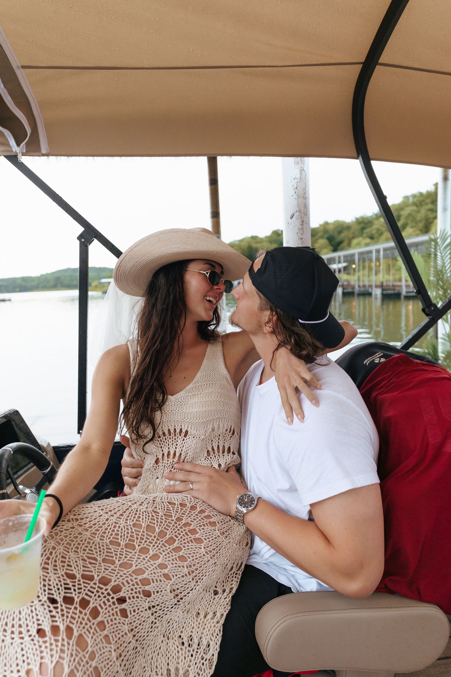 A couple sharing an intimate moment on a boat with a lake and shoreline in the background.