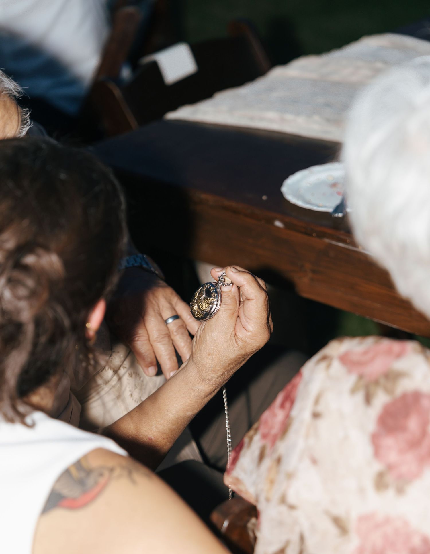 Someone examines a pocket watch or timepiece while sitting at a wooden table.
