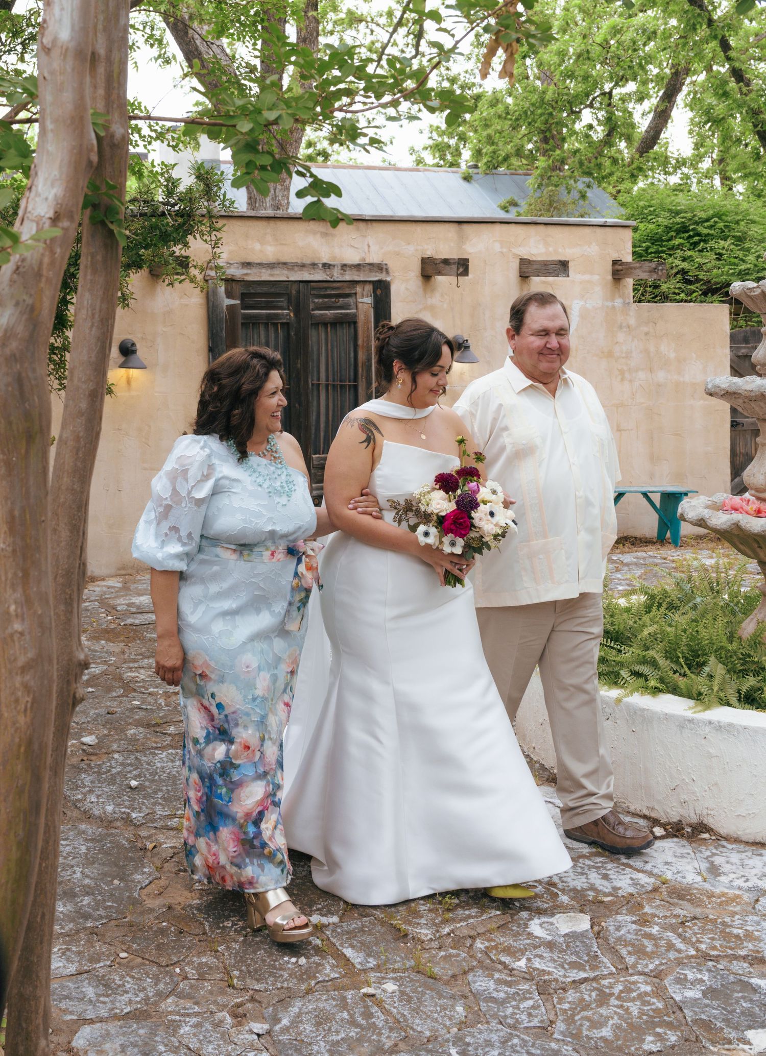 A group in formal attire gathers for a celebration under trees in a courtyard setting.