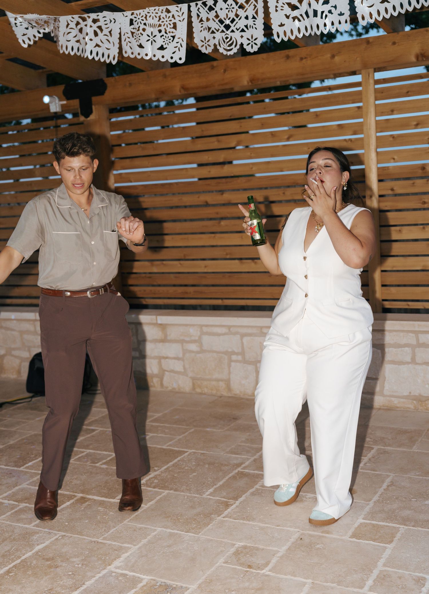 People in brown and white outfits perform a choreographed dance sequence on a tiled floor under decorative banners.