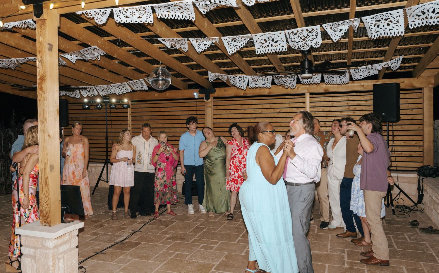 A rustic barn wedding reception venue decorated with white bunting and string lights showing guests dancing on the wooden floor.