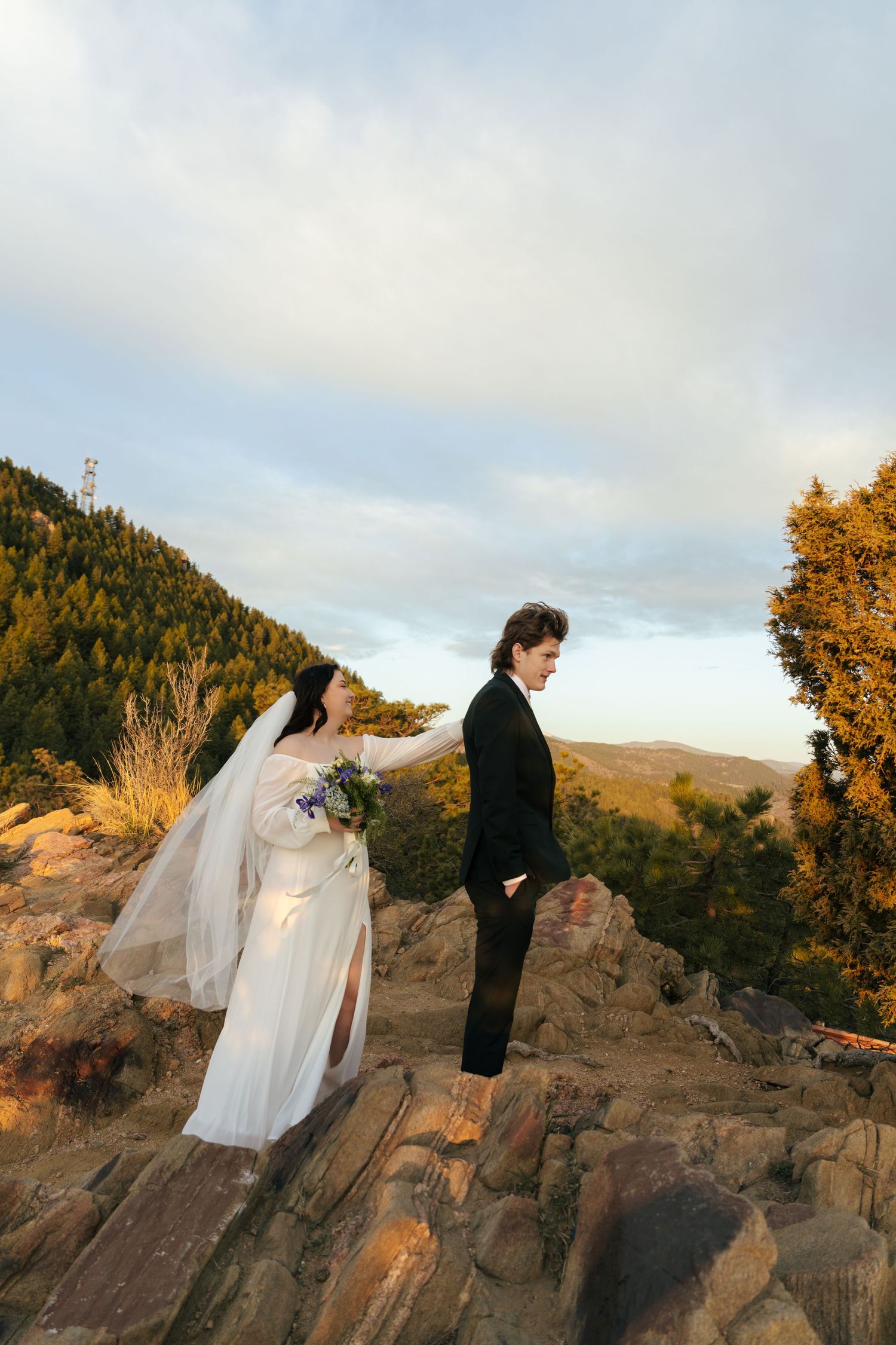 A bride and groom pose for romantic sunset photos on dramatic rocky cliffs.