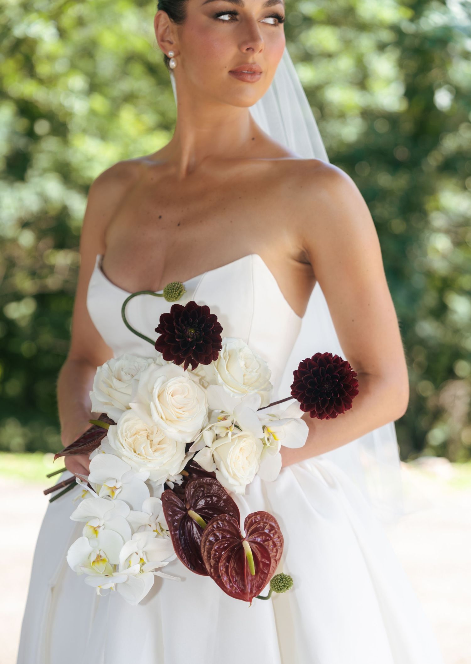 Elegant bridal bouquet featuring white roses, burgundy dahlias and orchids against a white wedding dress.
