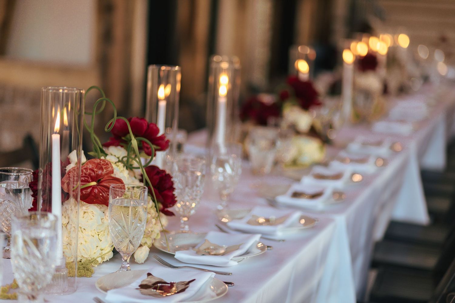 Long banquet tables decorated with burgundy and cream floral arrangements for an upscale wedding reception.