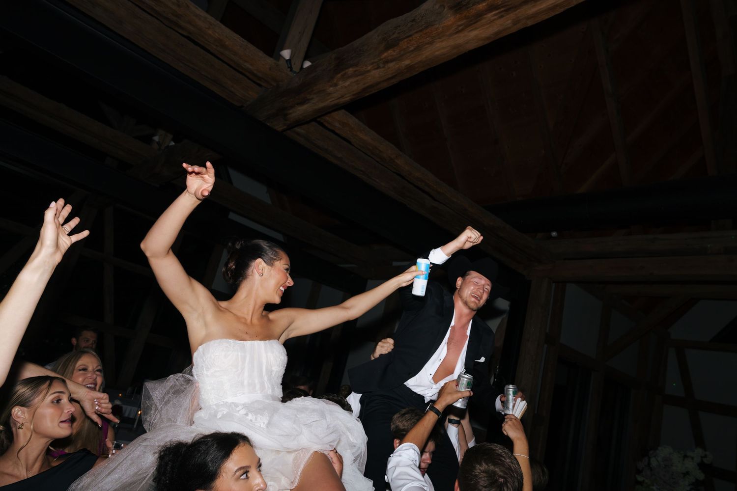 People dancing and celebrating with raised arms in a rustic venue with wooden beams.