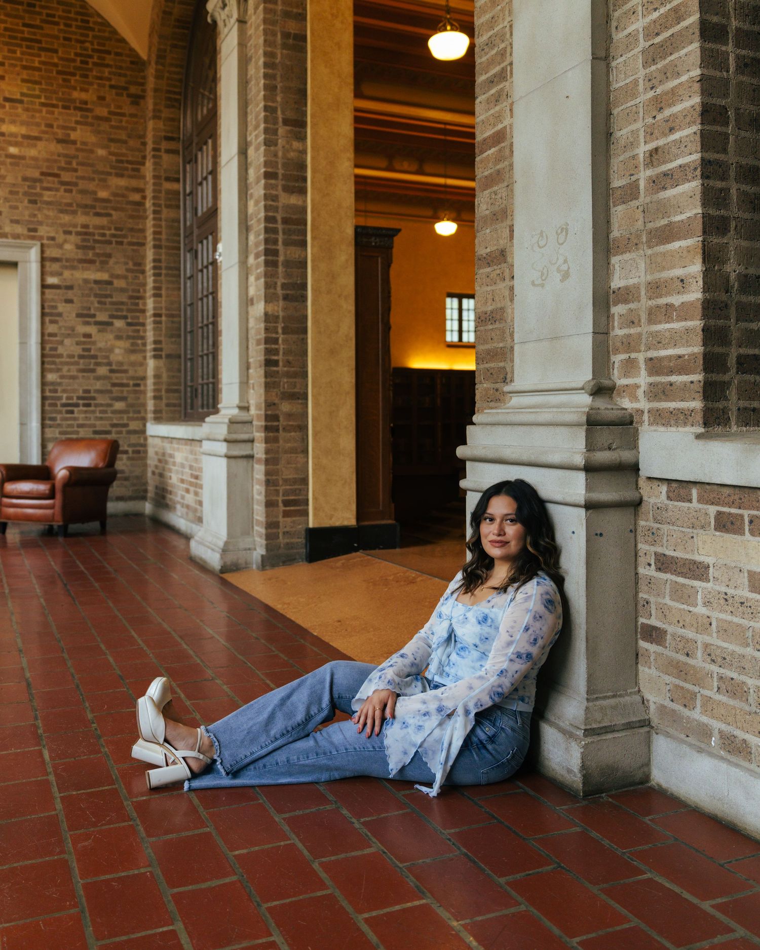 A figure rests along a brick corridor with arched columns and terracotta floors in an architectural setting.