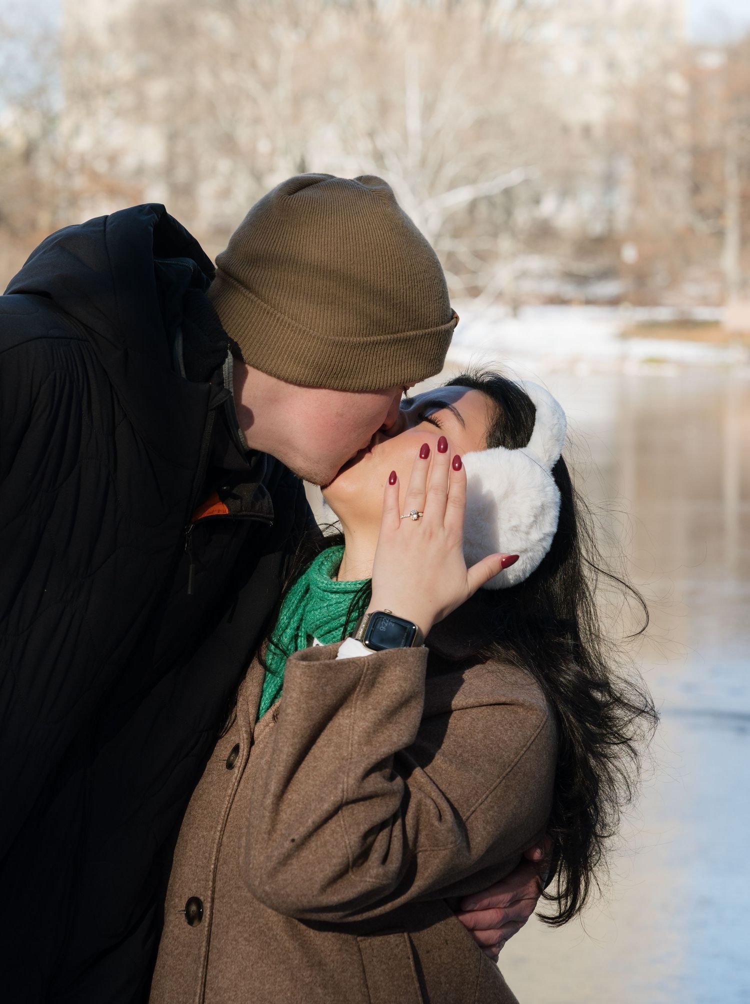 Two people embrace and kiss near a snow-covered lake in winter.