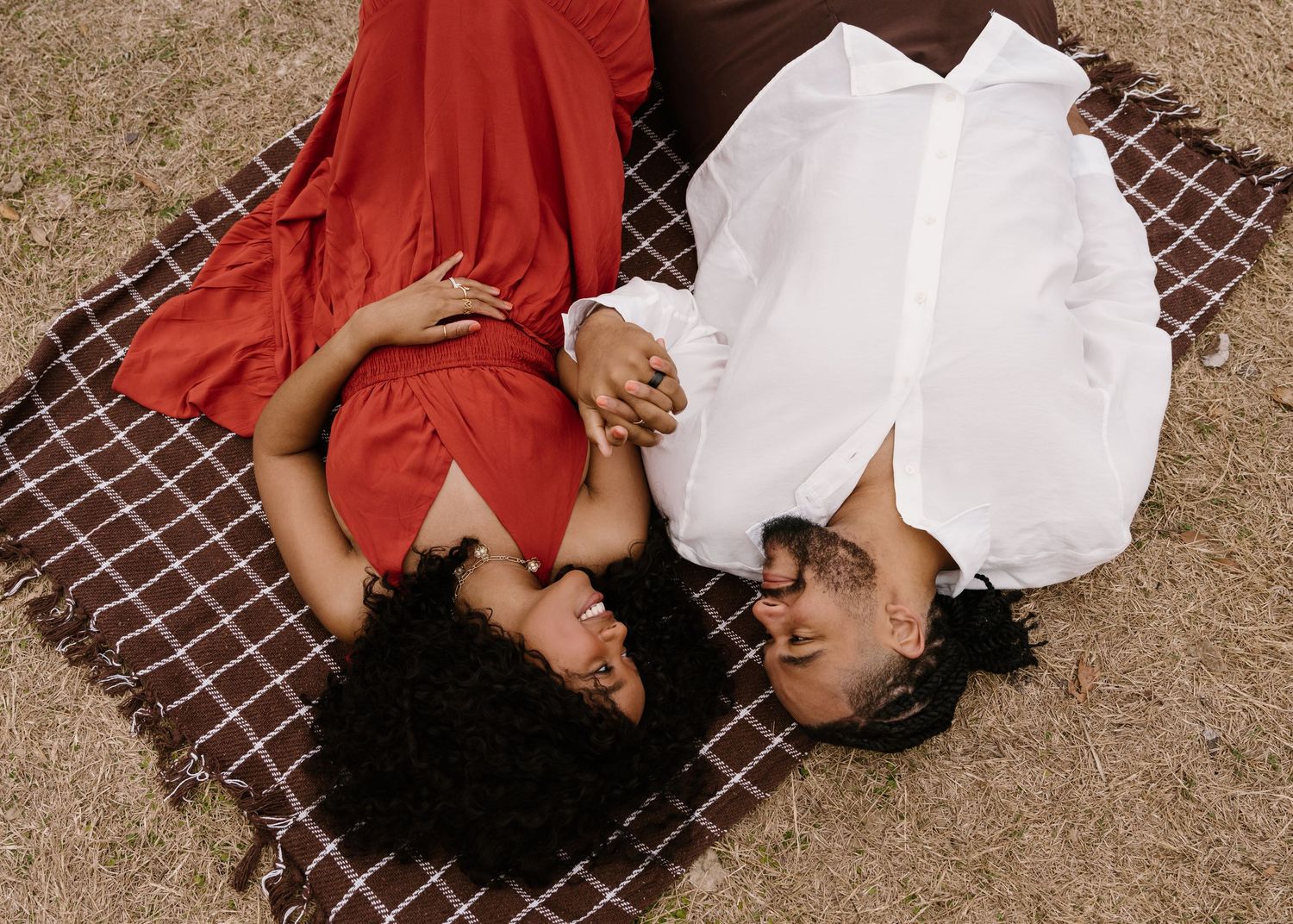 Two people lying on a plaid blanket wearing red and white outfits while sharing a tender moment.