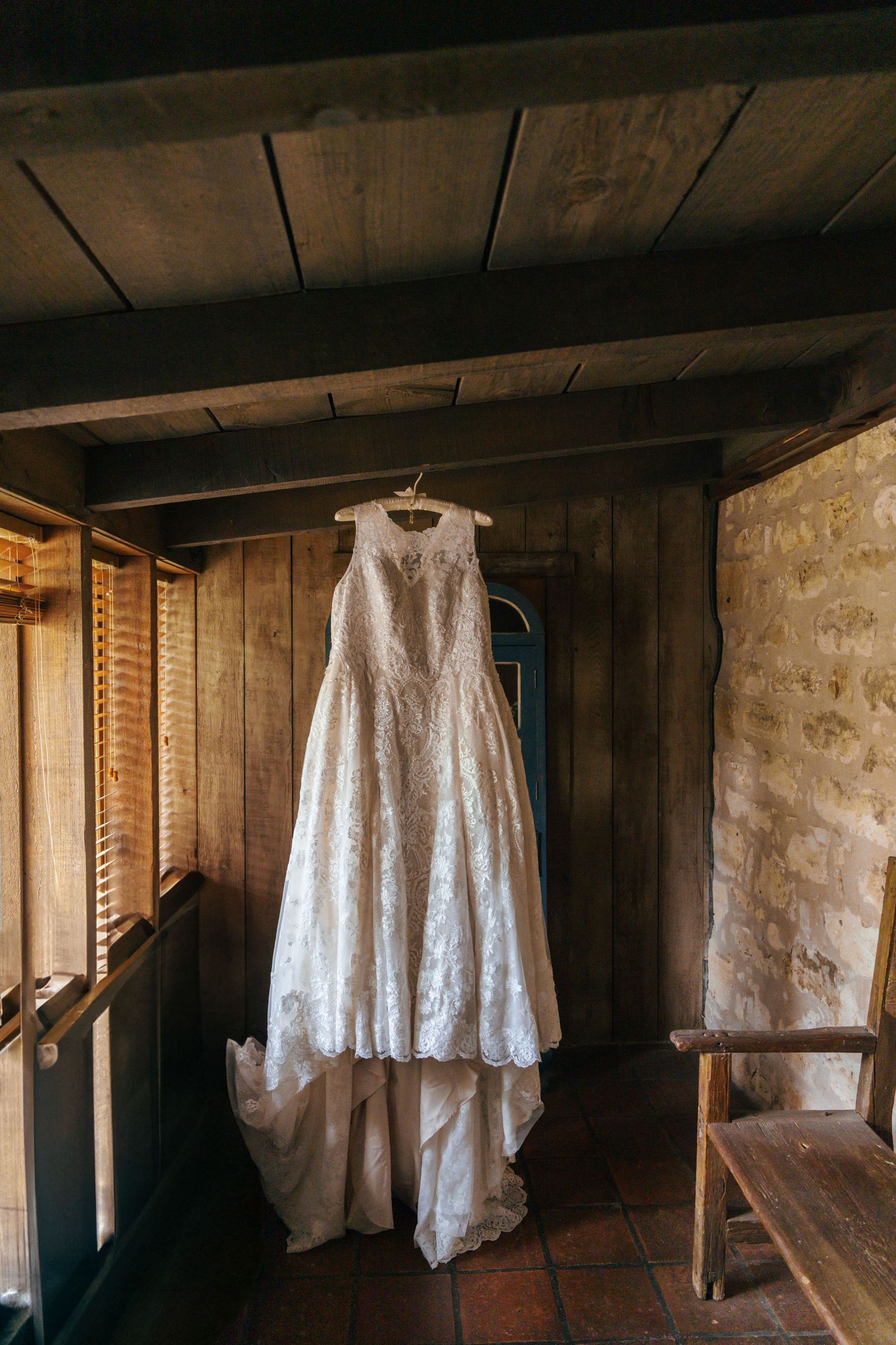 Vintage white lace dresses hanging in a rustic wooden attic with stone walls and natural lighting.
