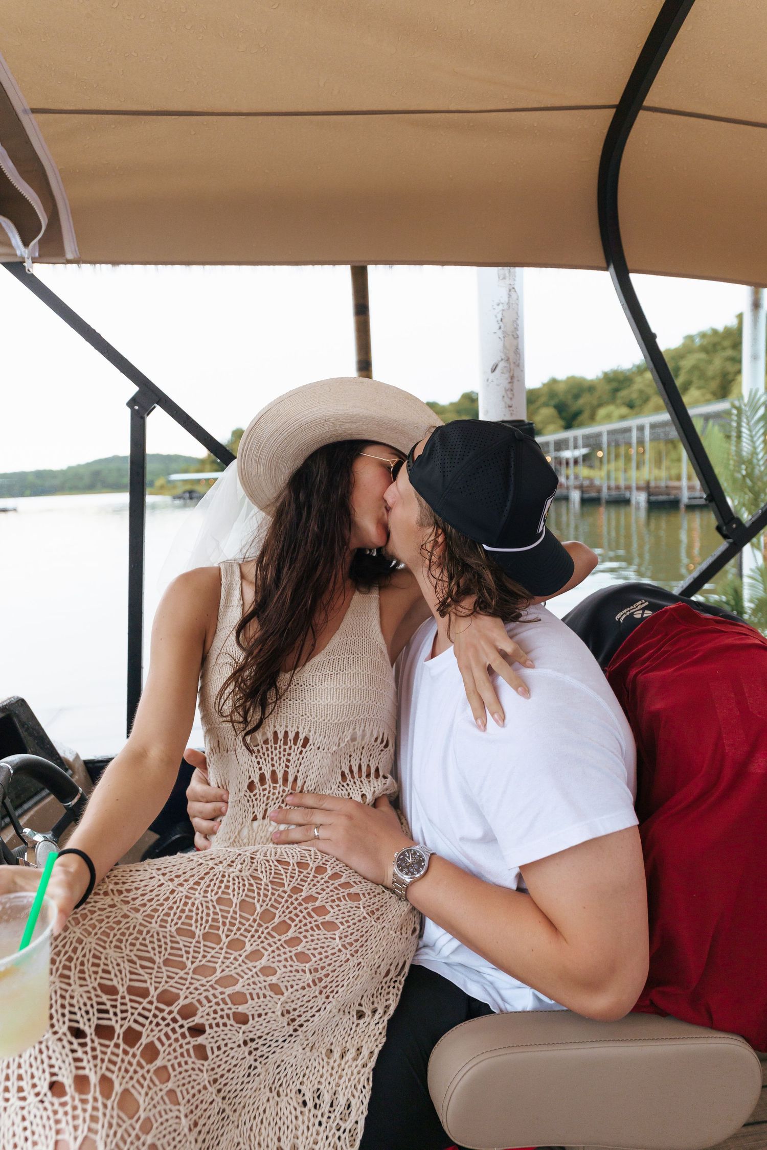 Couple sharing intimate moment on boat with lake and docks in background.