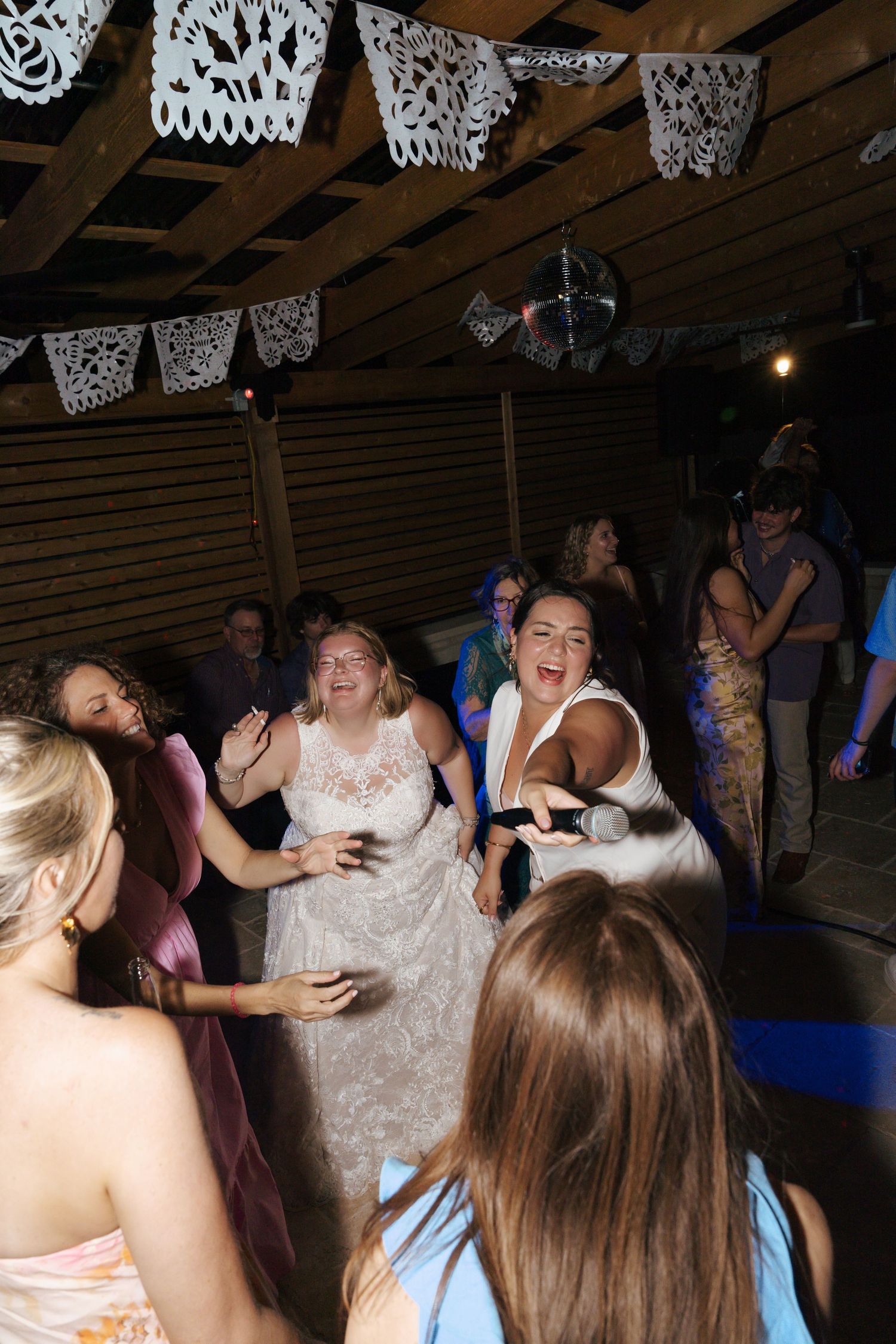 People dancing and celebrating at a wedding reception under white papel picado decorations.