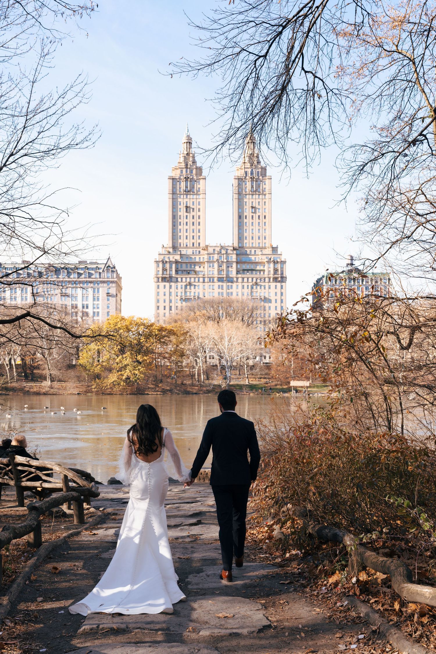A couple walks along the scenic path by the lake in Central Park with iconic Manhattan buildings in autumn.