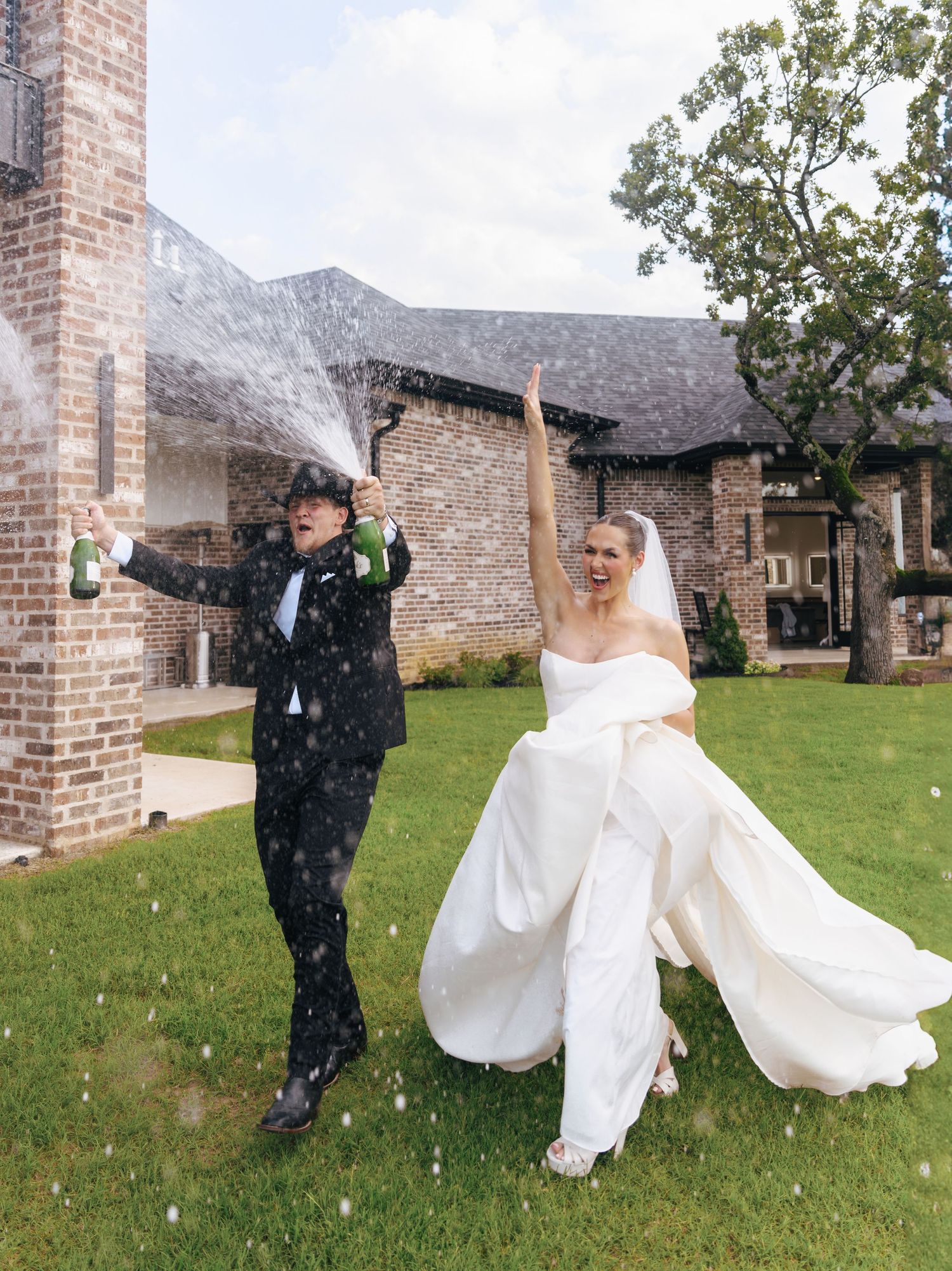 A joyful wedding celebration with the couple dancing outdoors near a brick building as confetti falls around them.