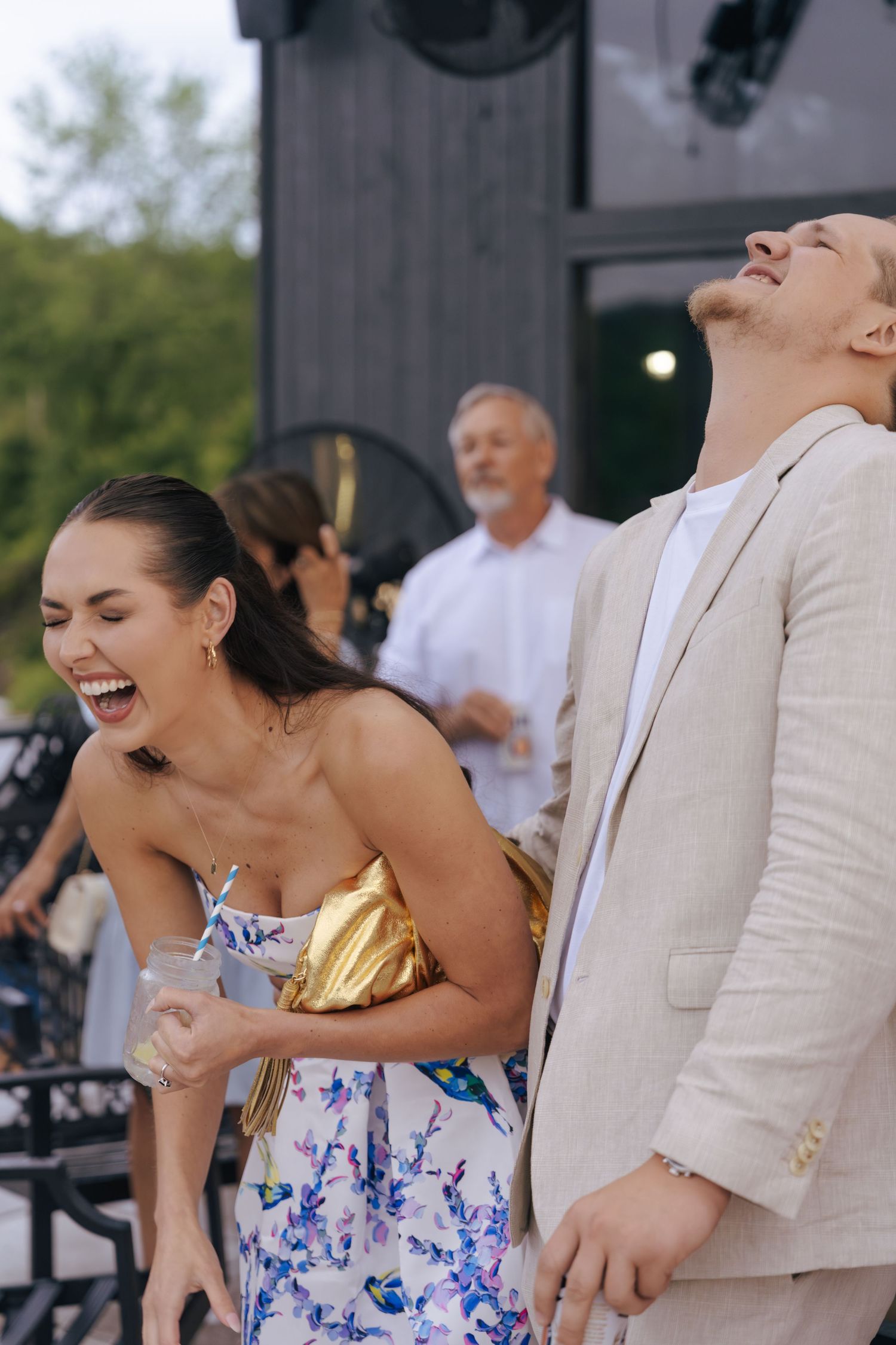 A couple shares a joyful moment together during an outdoor event, with the woman wearing a blue and white floral dress.