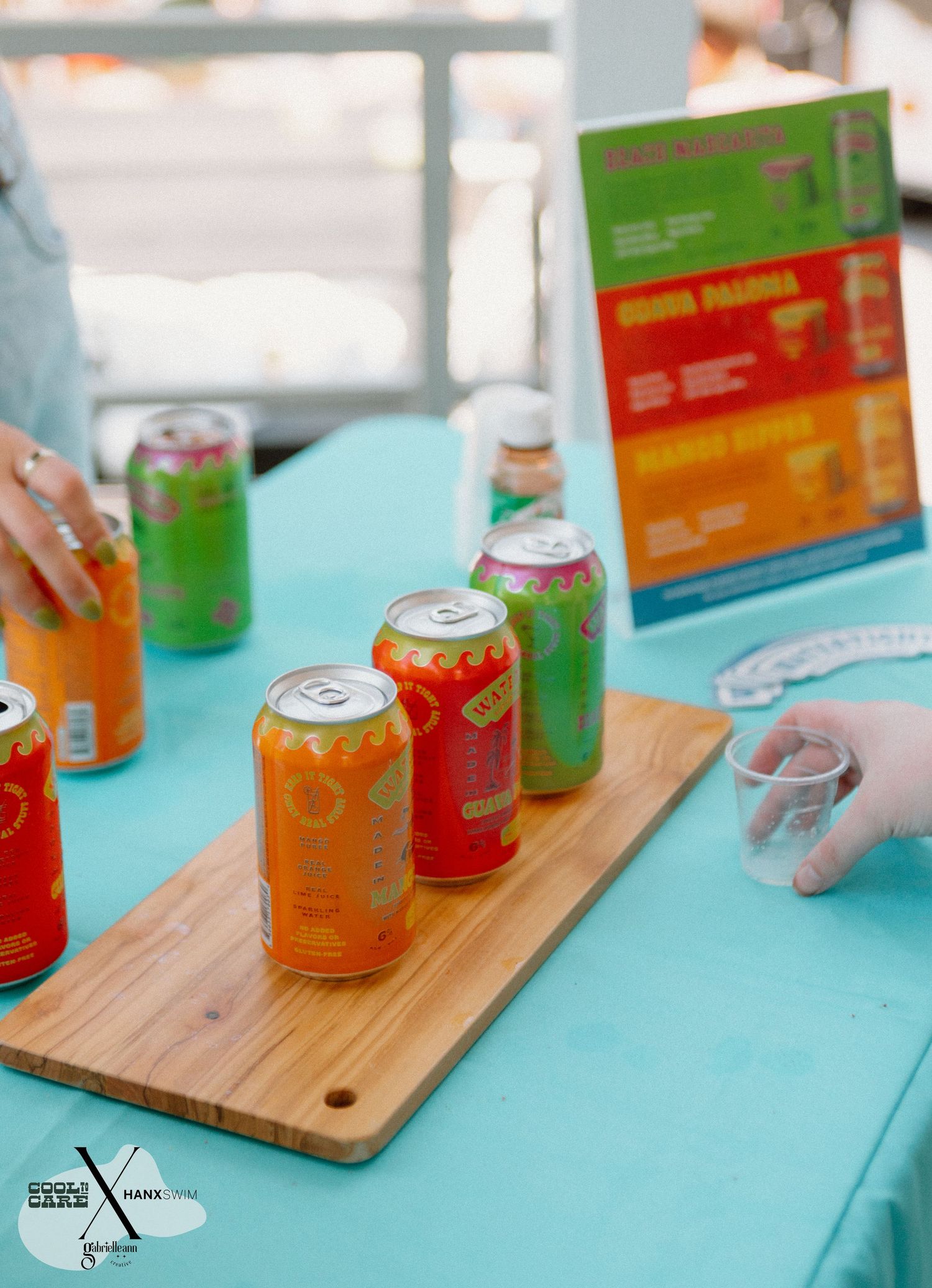 Orange and green beverage cans arranged on wooden cutting board with turquoise background.