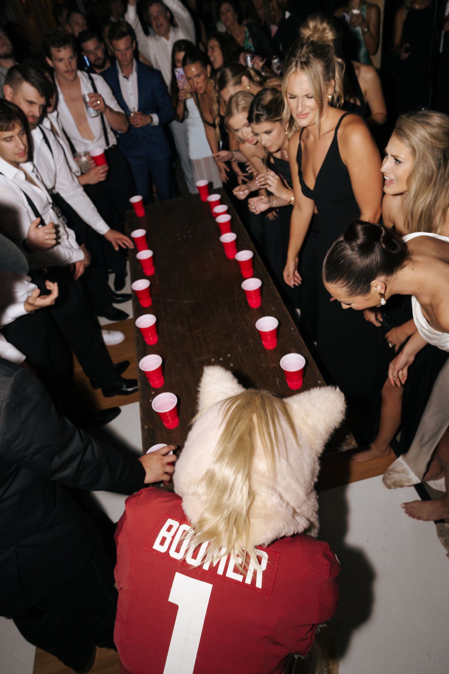 Wedding party plays beer pong game with red cups at reception.