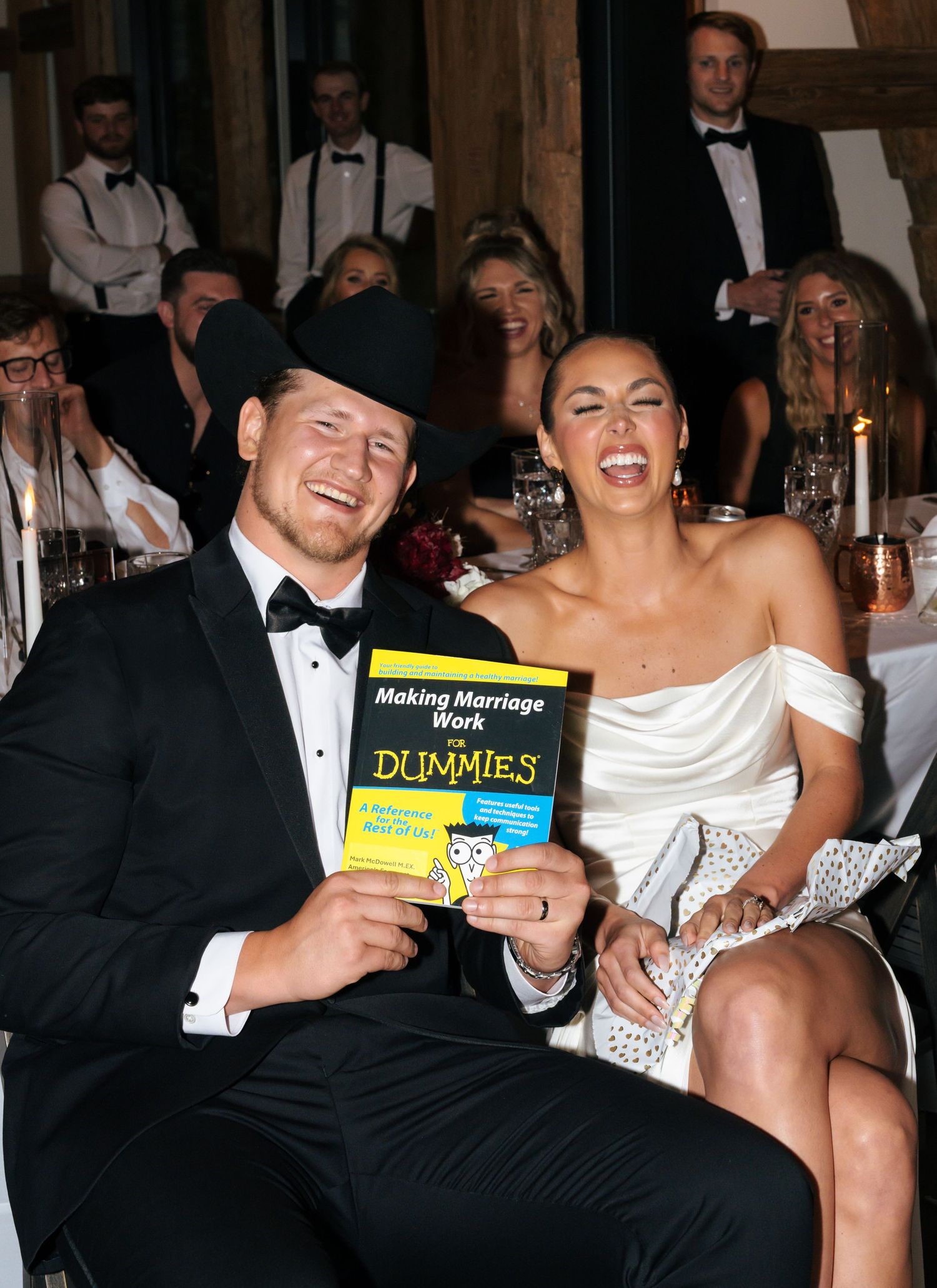 Couple shares humorous moment with 'For Dummies' book at wedding reception.