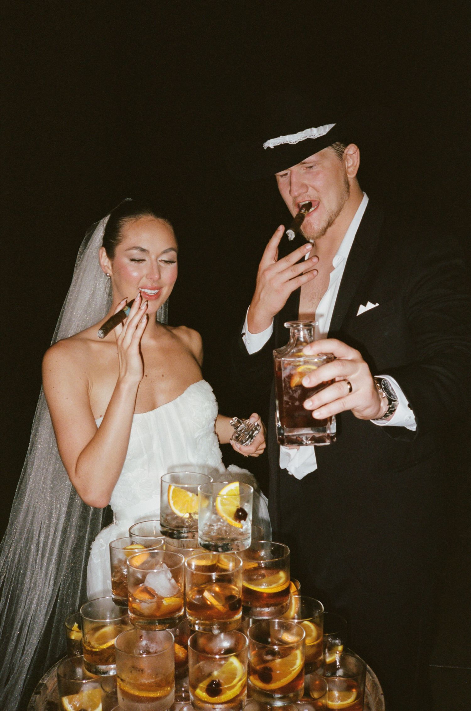 Wedding couple enjoying drinks at reception with pyramid of cocktail glasses.
