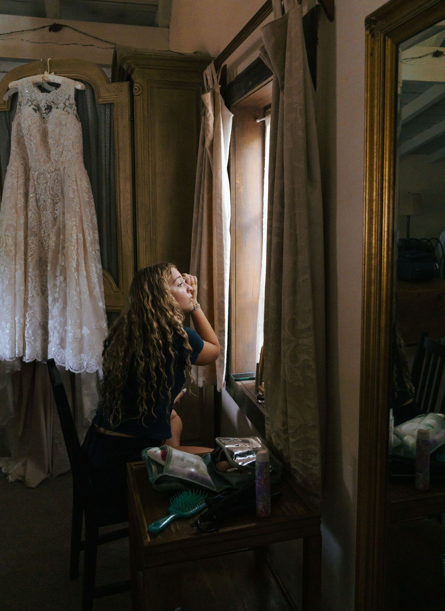 A series of moody photographs showing a white lace dress hanging in a dimly lit room with window light.