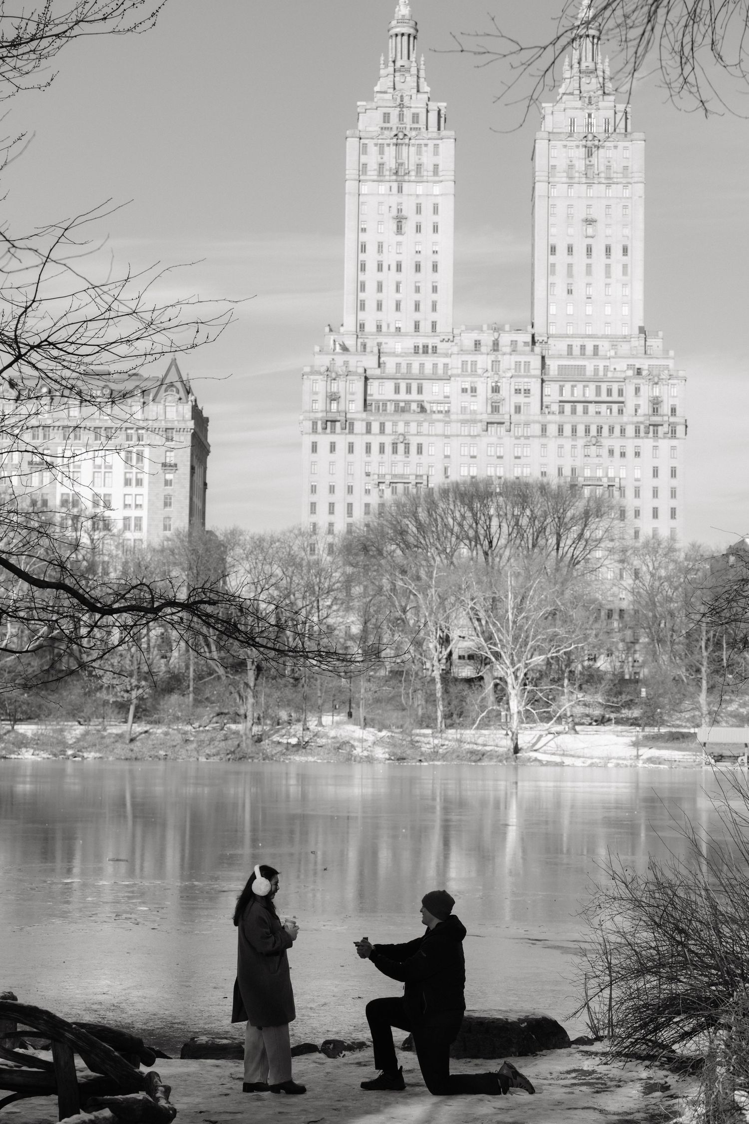 Silhouettes of people by a lake with art deco buildings in the background at Central Park, New York City.