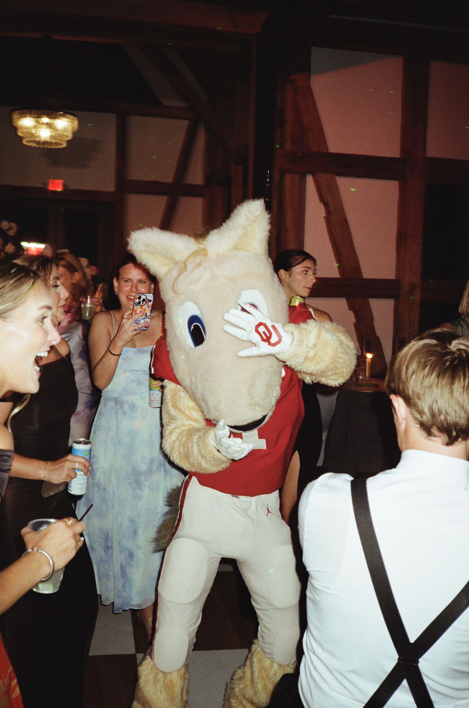 People dancing with a large mascot character at a lively indoor reception party.
