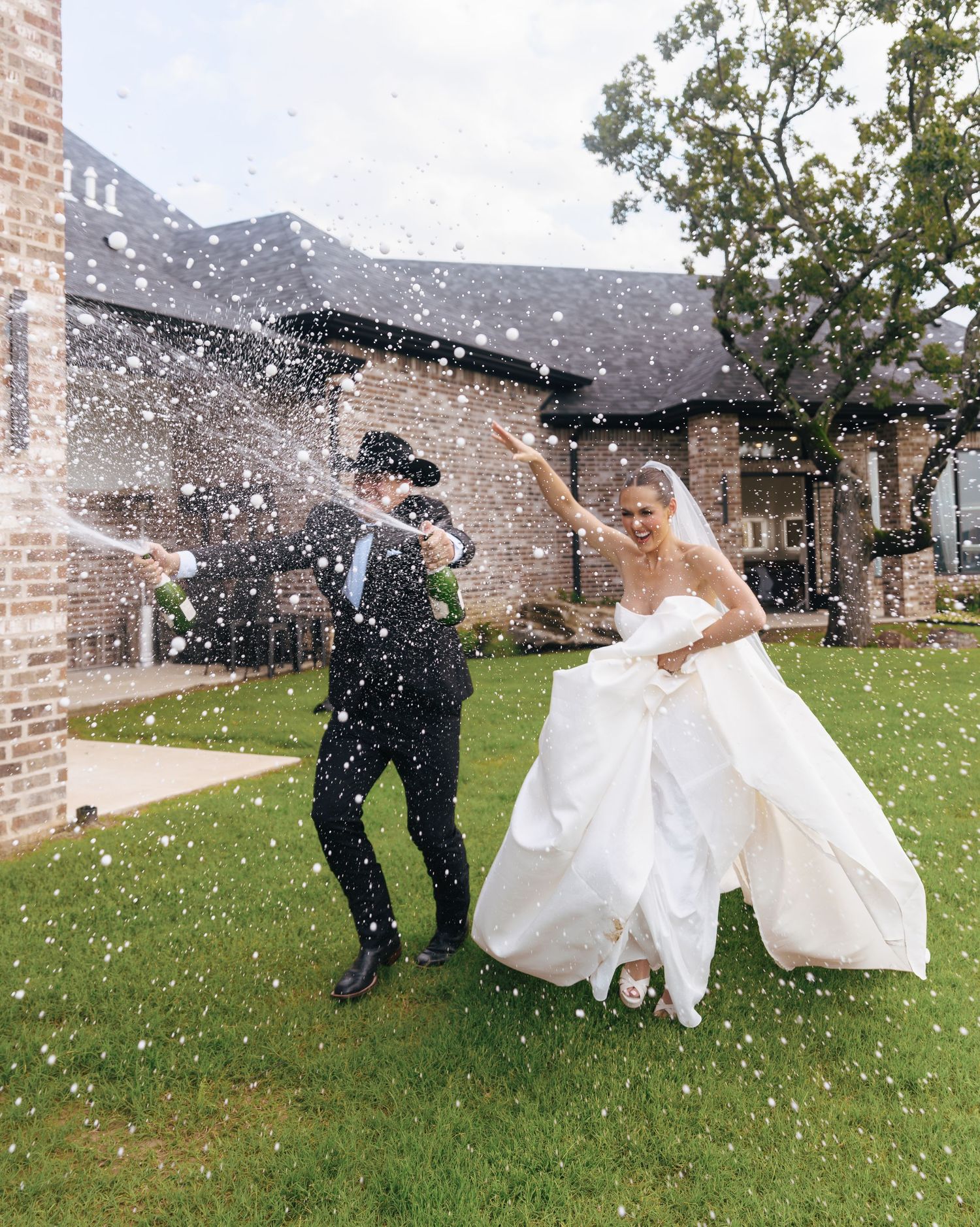 Playful wedding photo with confetti flying around the couple on a grassy lawn.