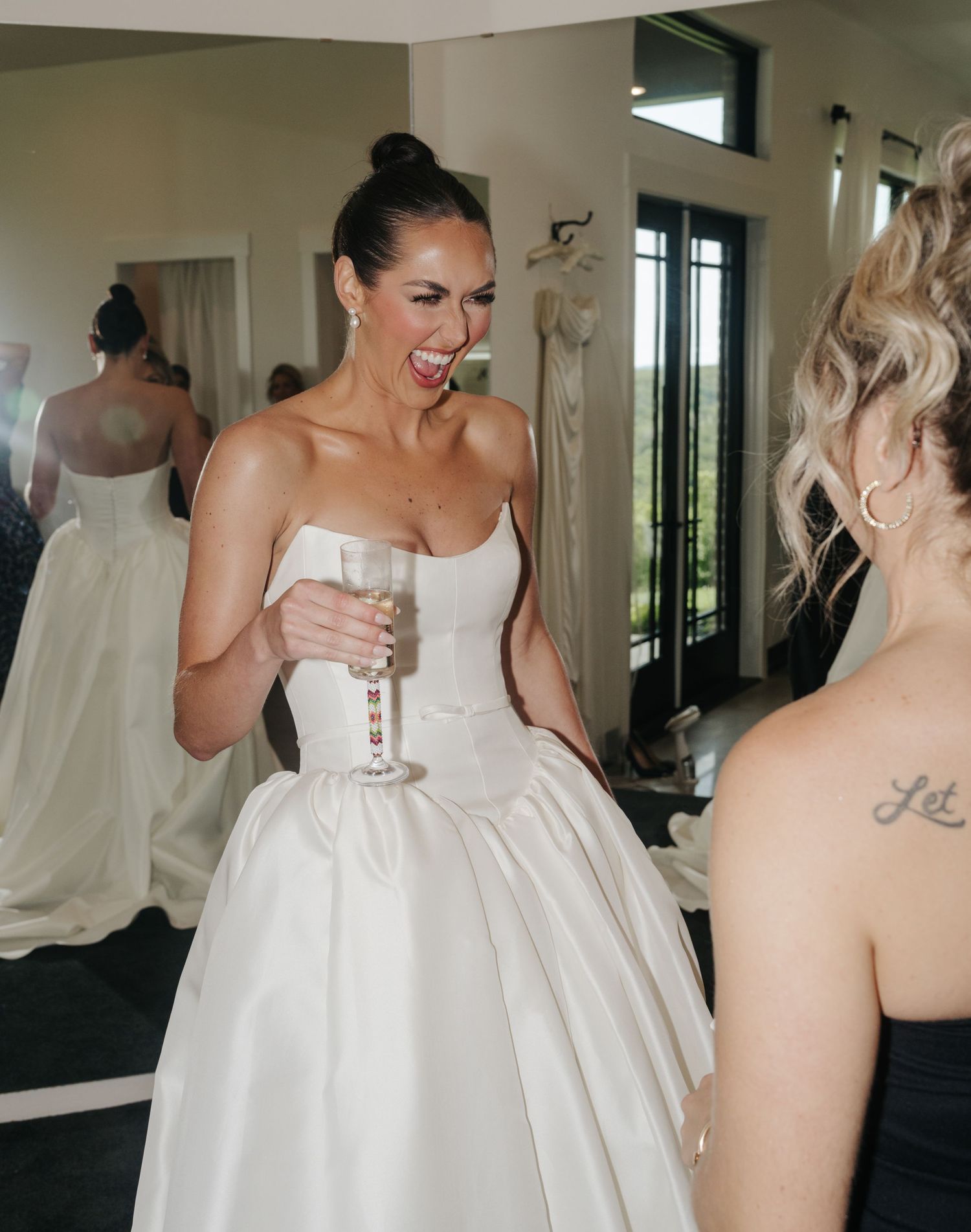 Candid moment of a bride in a white ballgown dress holding a champagne glass during wedding preparations.