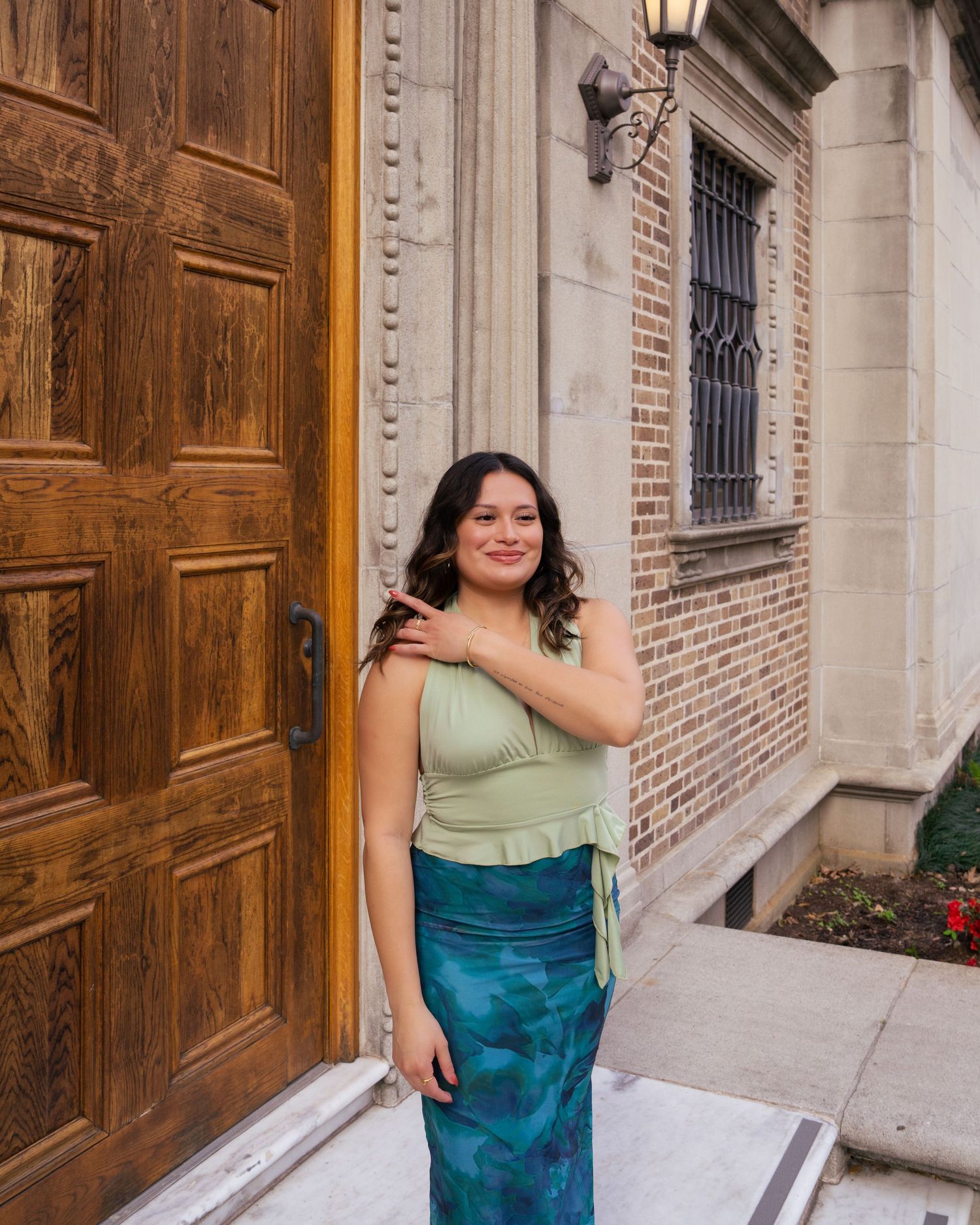 Woman in turquoise dress poses in front of ornate wooden doors and brick building facade.