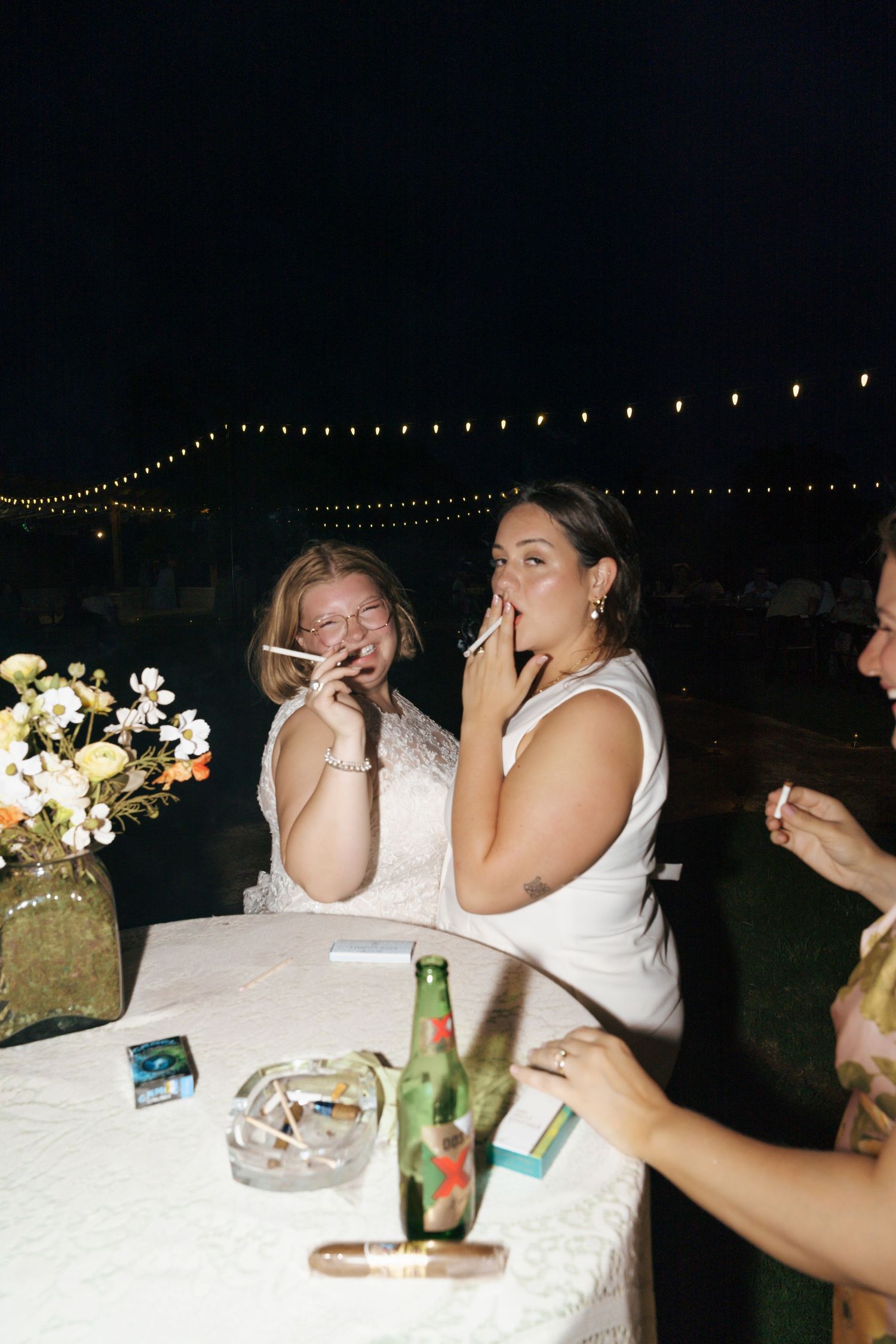 A group of people laugh and enjoy themselves at a nighttime outdoor event with string lights visible overhead.